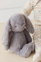 Grey plush bunny toy and baby in floral pajamas.
