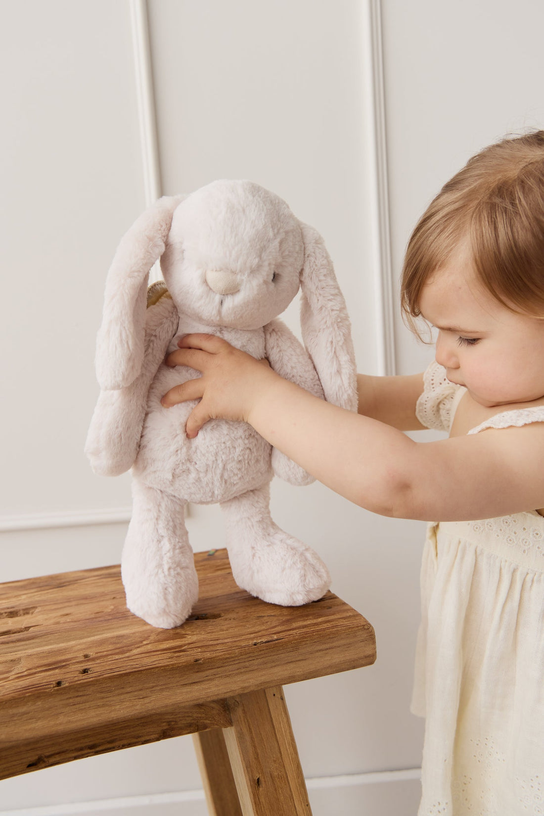 Child with a plush bunny on a wooden stool.