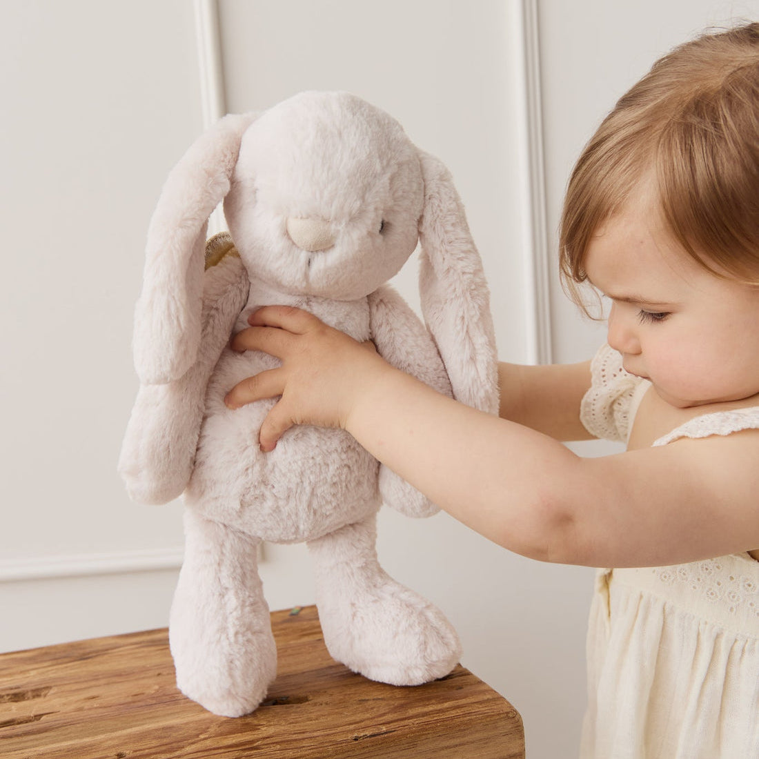 Child with a plush bunny on a wooden stool.