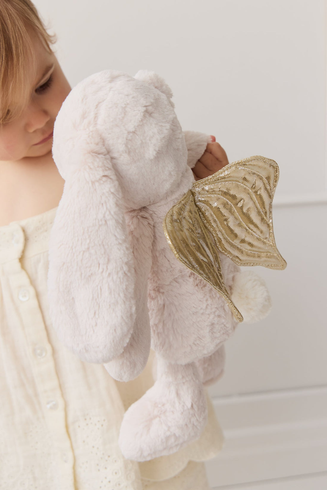 Child holding a plush bunny toy with golden wings.