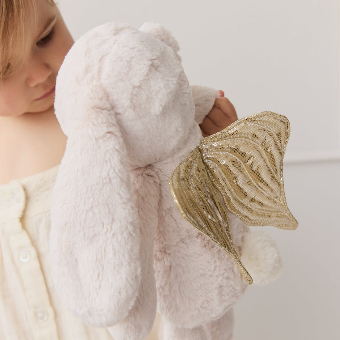 Child holding a plush bunny toy with golden wings.