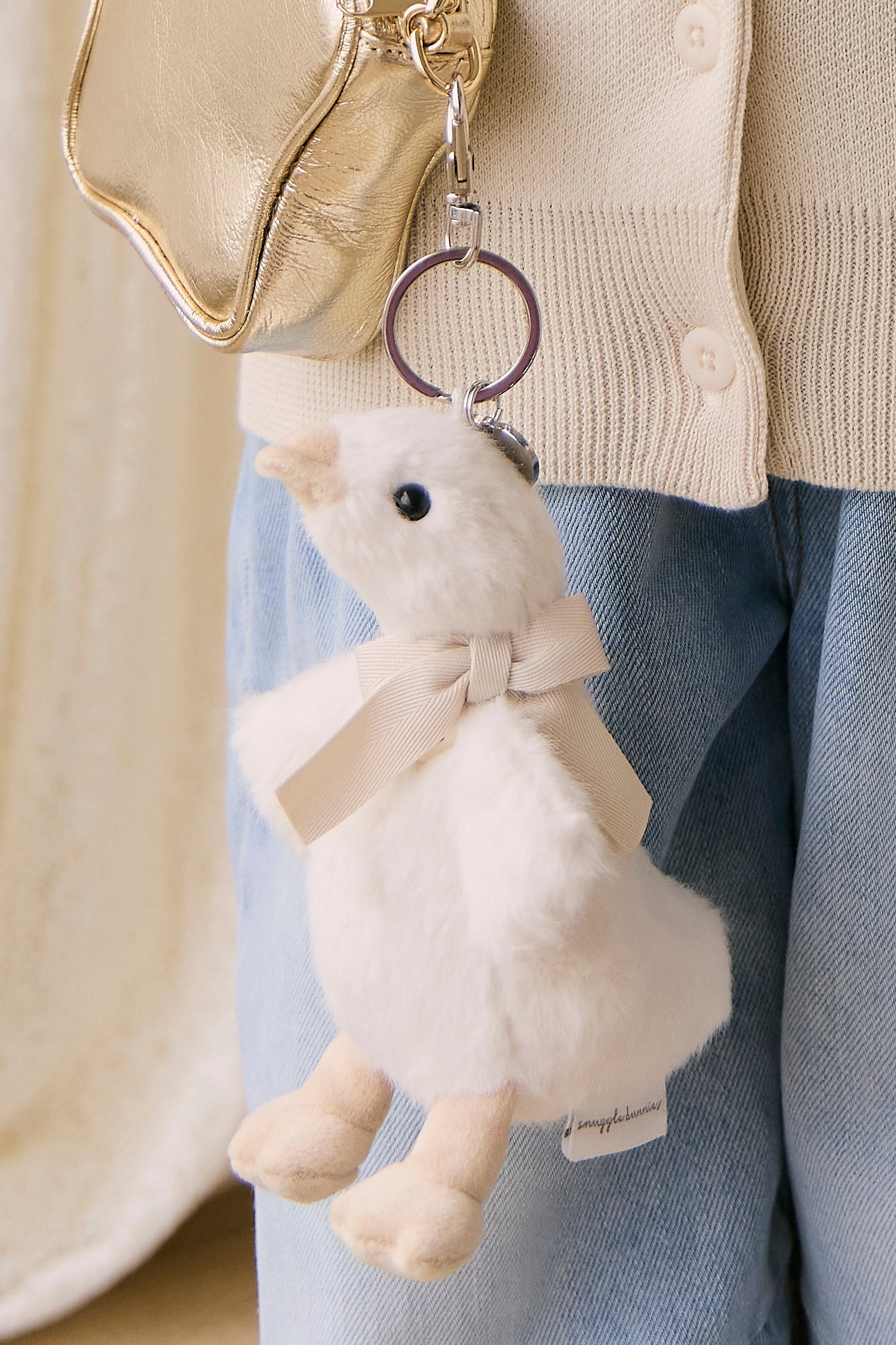 White plush keychain with a bow attached to a gold bag.