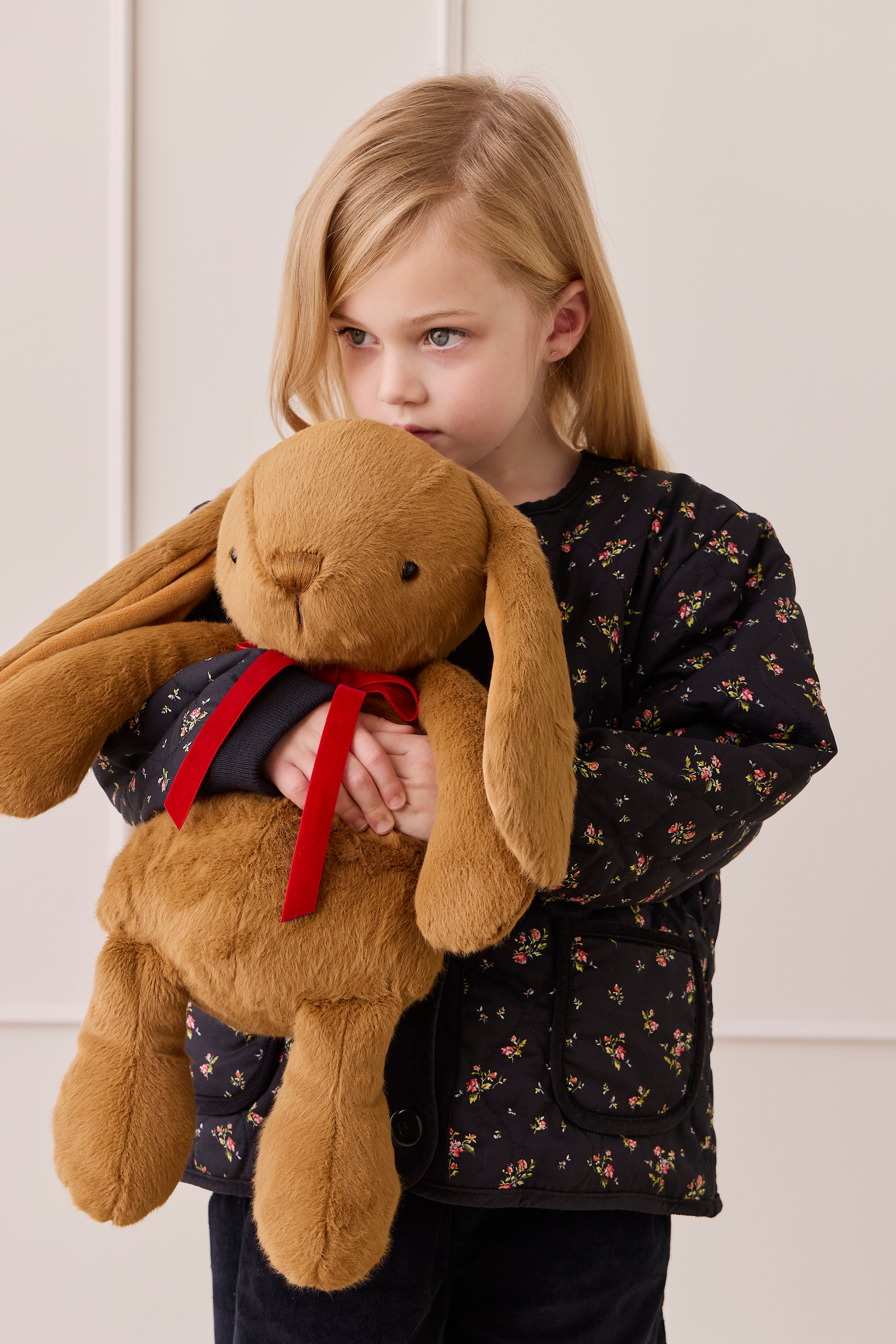 Child holding a large brown teddy bear with a red bow against a light background