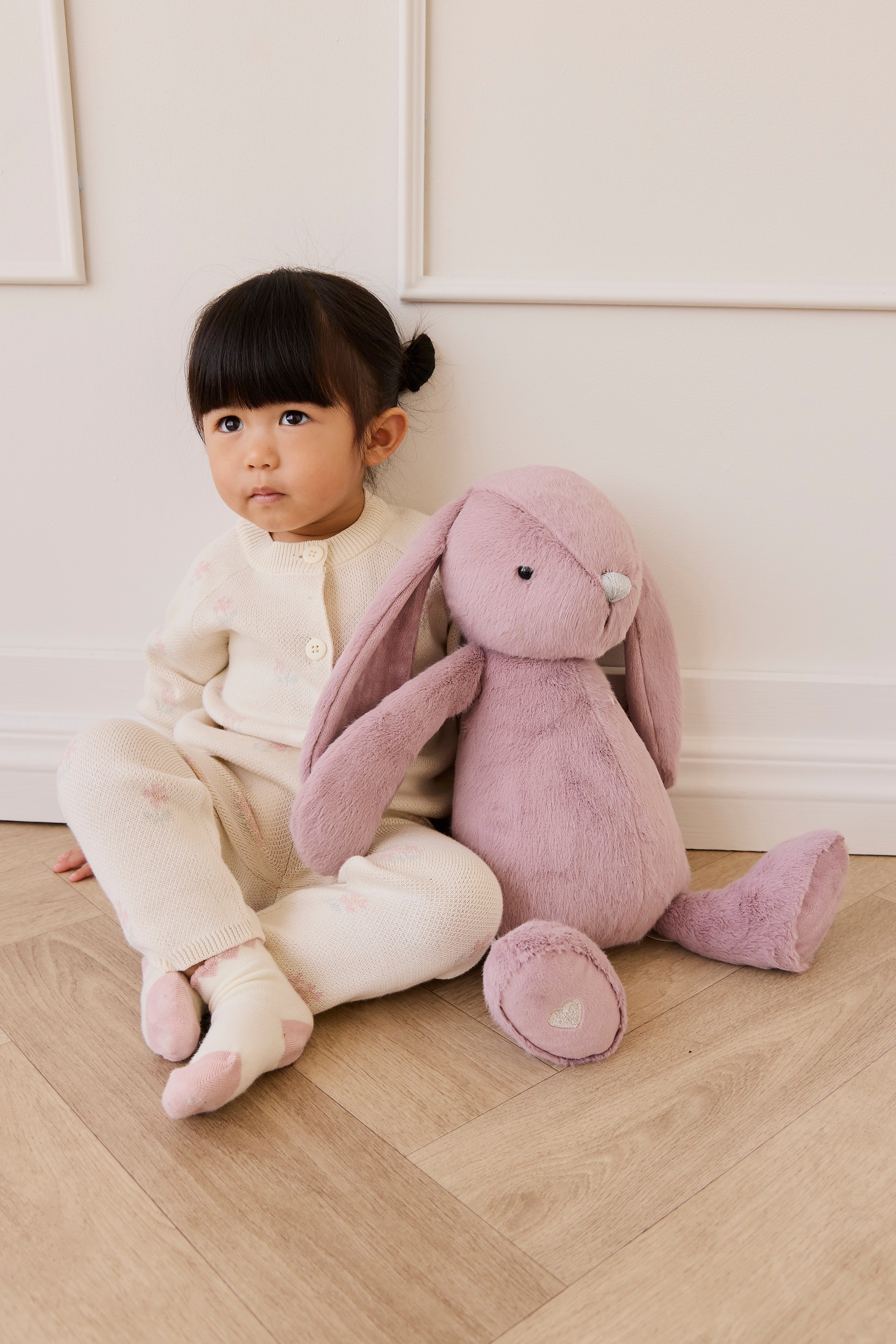 Child sitting on a wooden floor with a large pink plush toy