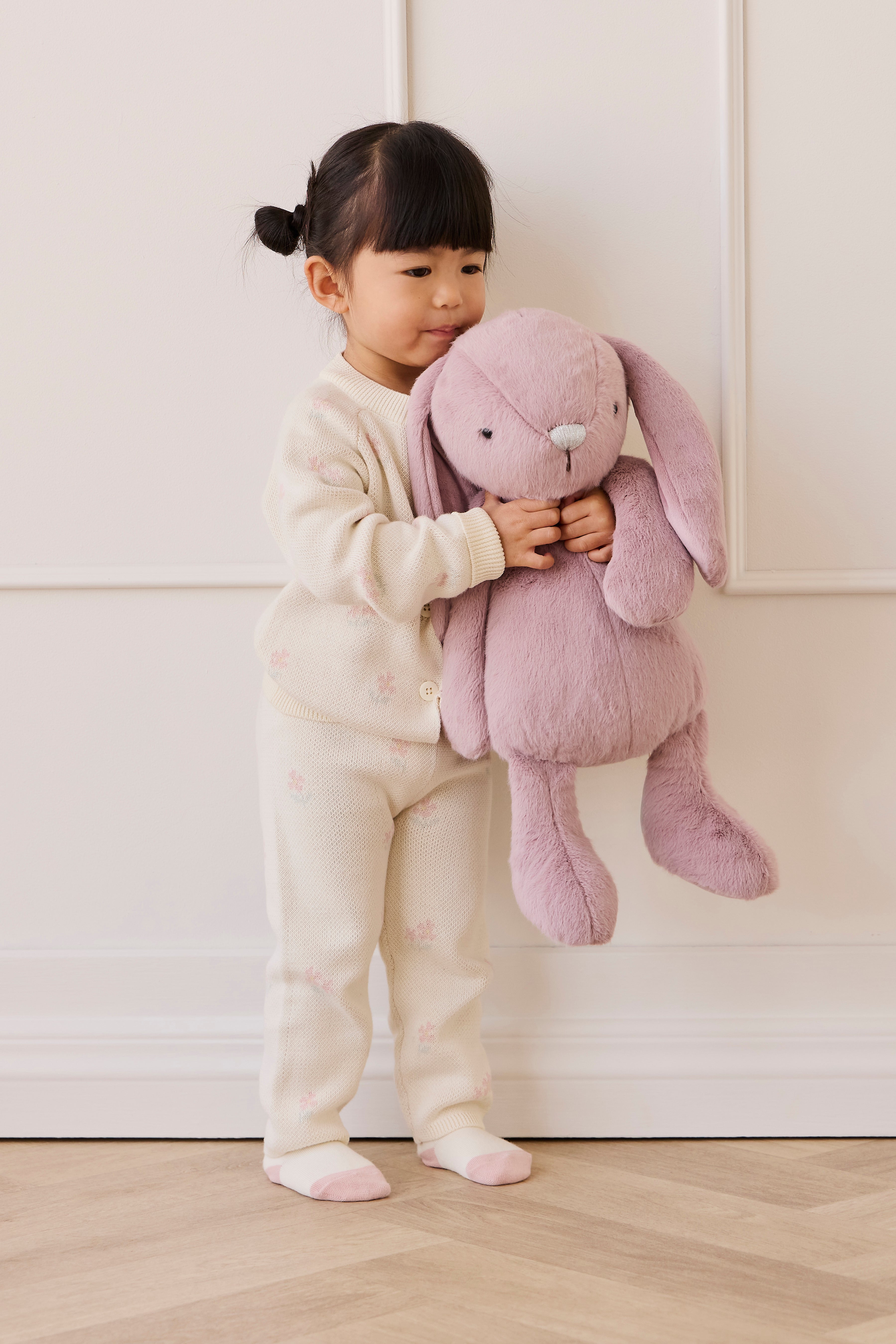 Child holding a pink plush bunny toy against a white background