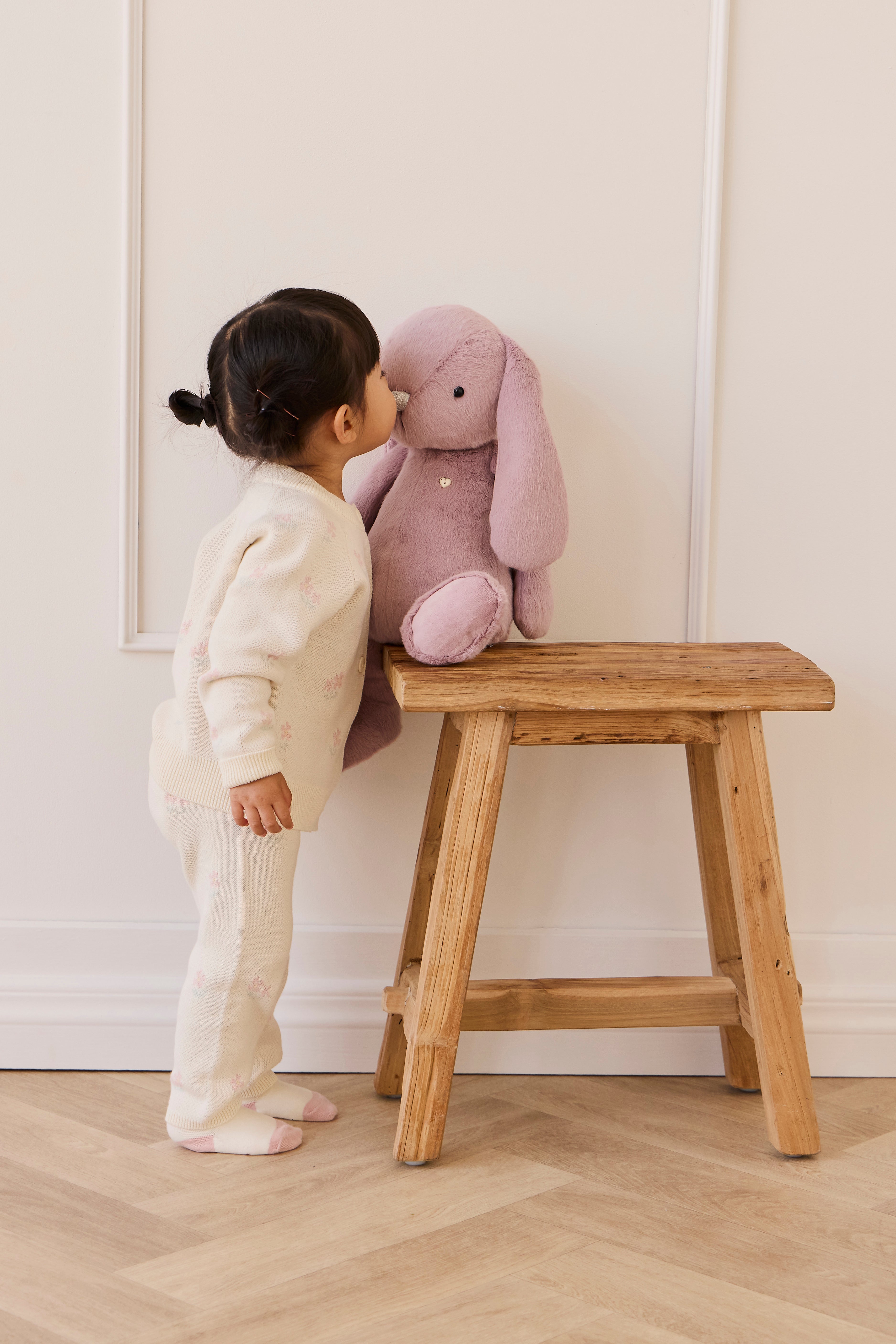 Child playing with a plush toy on a wooden stool against a white wall.