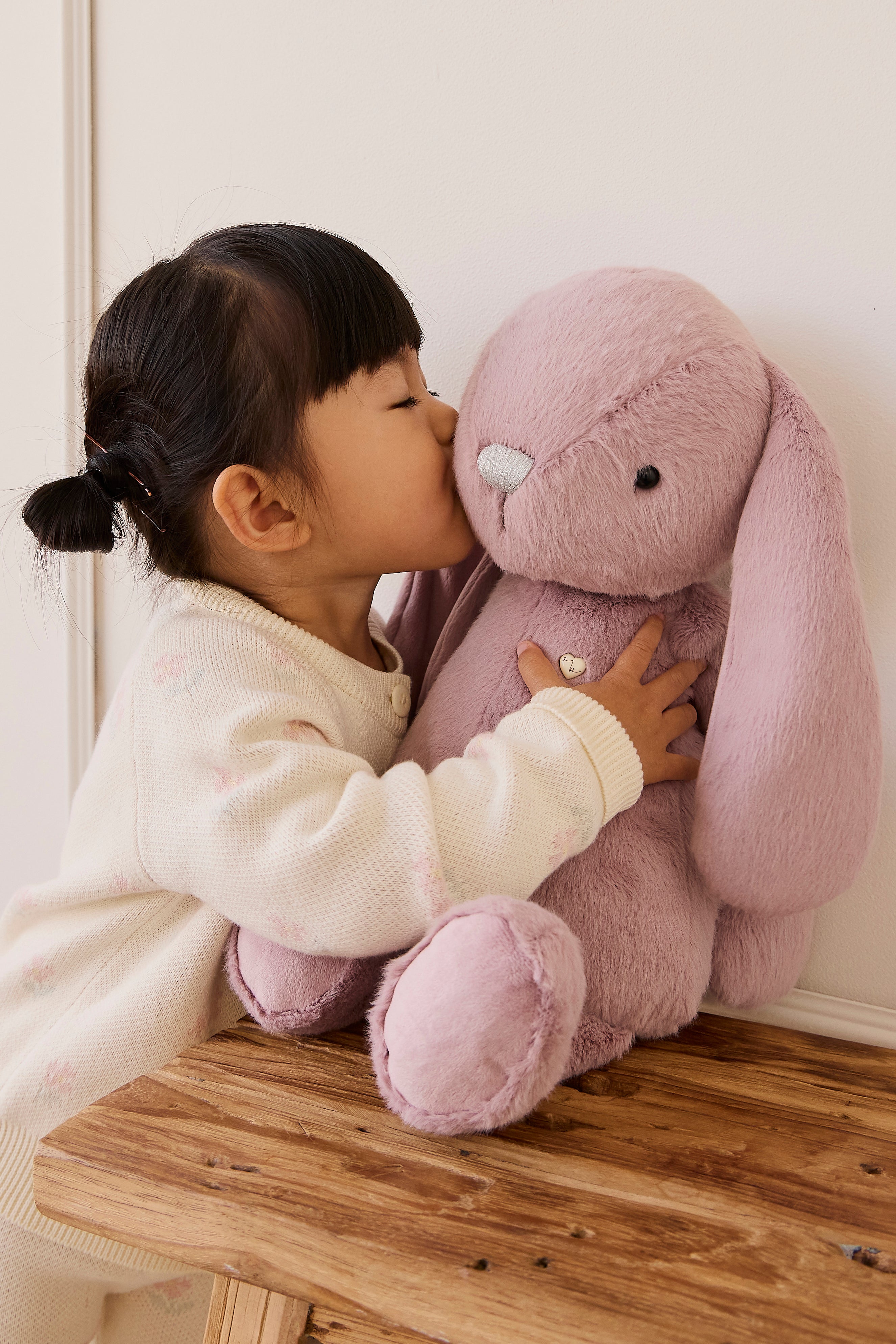 Child kissing a pink plush bunny toy on a wooden surface