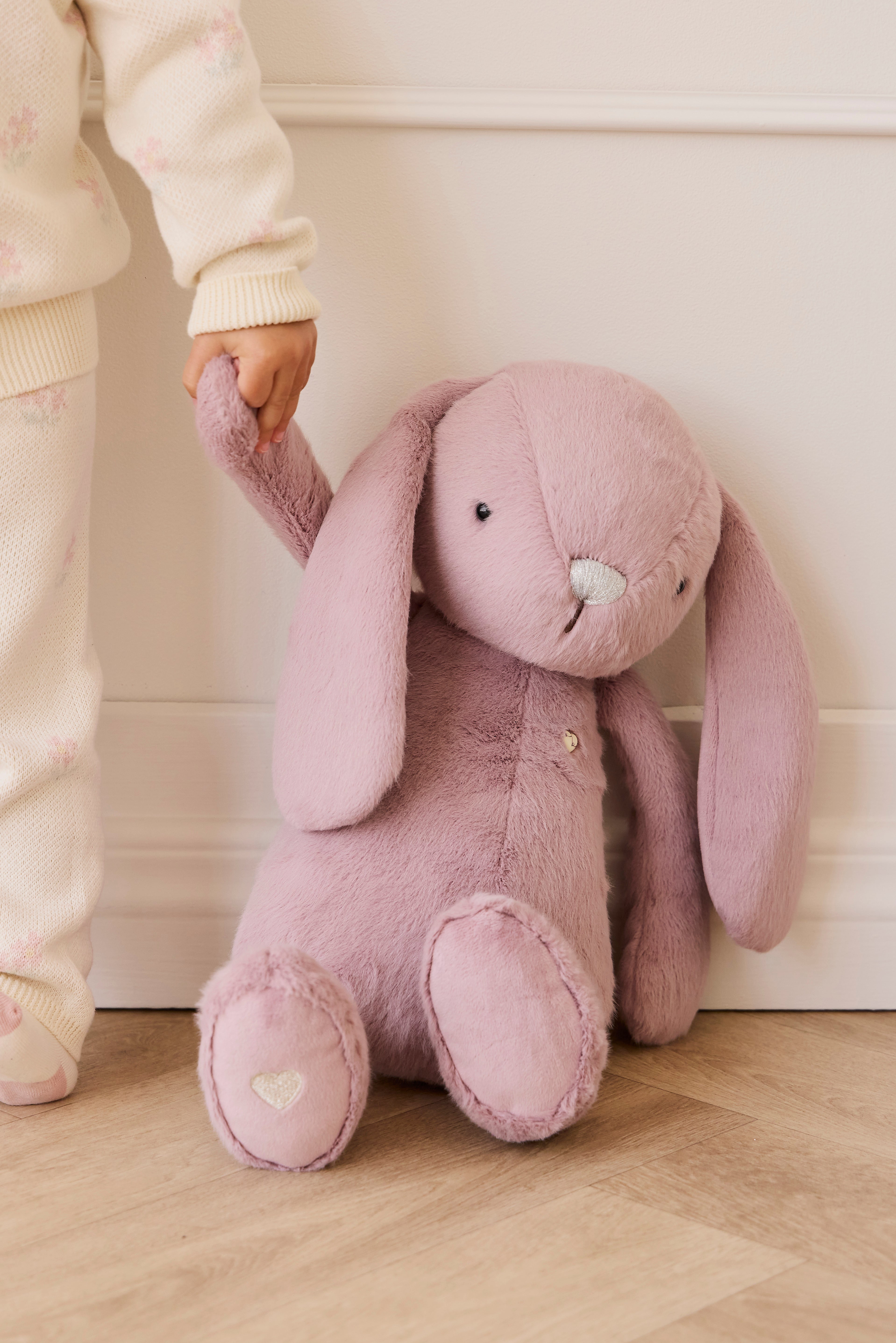 Child holding a large pink plush bunny toy against a white wall.