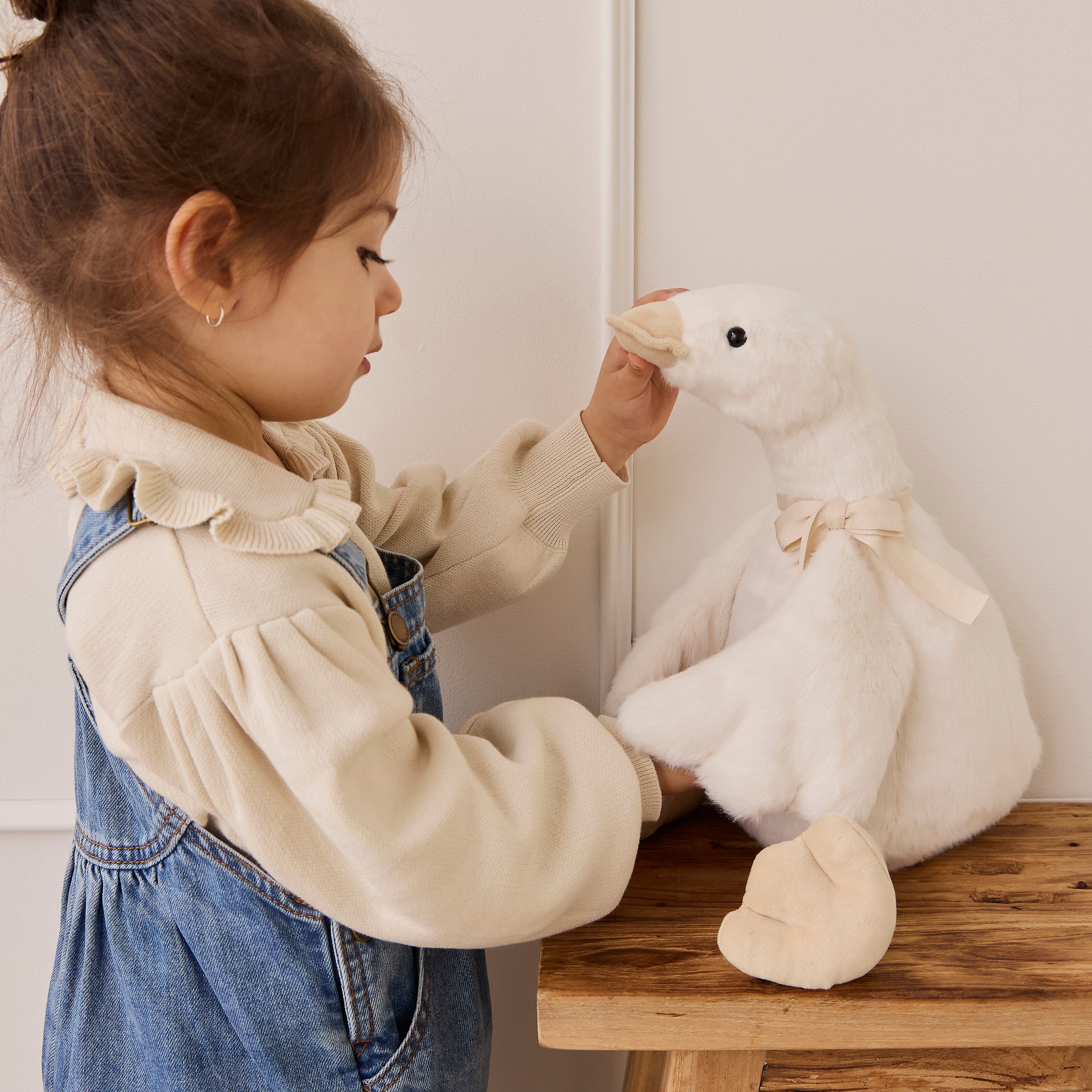 Child playing with a plush duck toy on a wooden table.