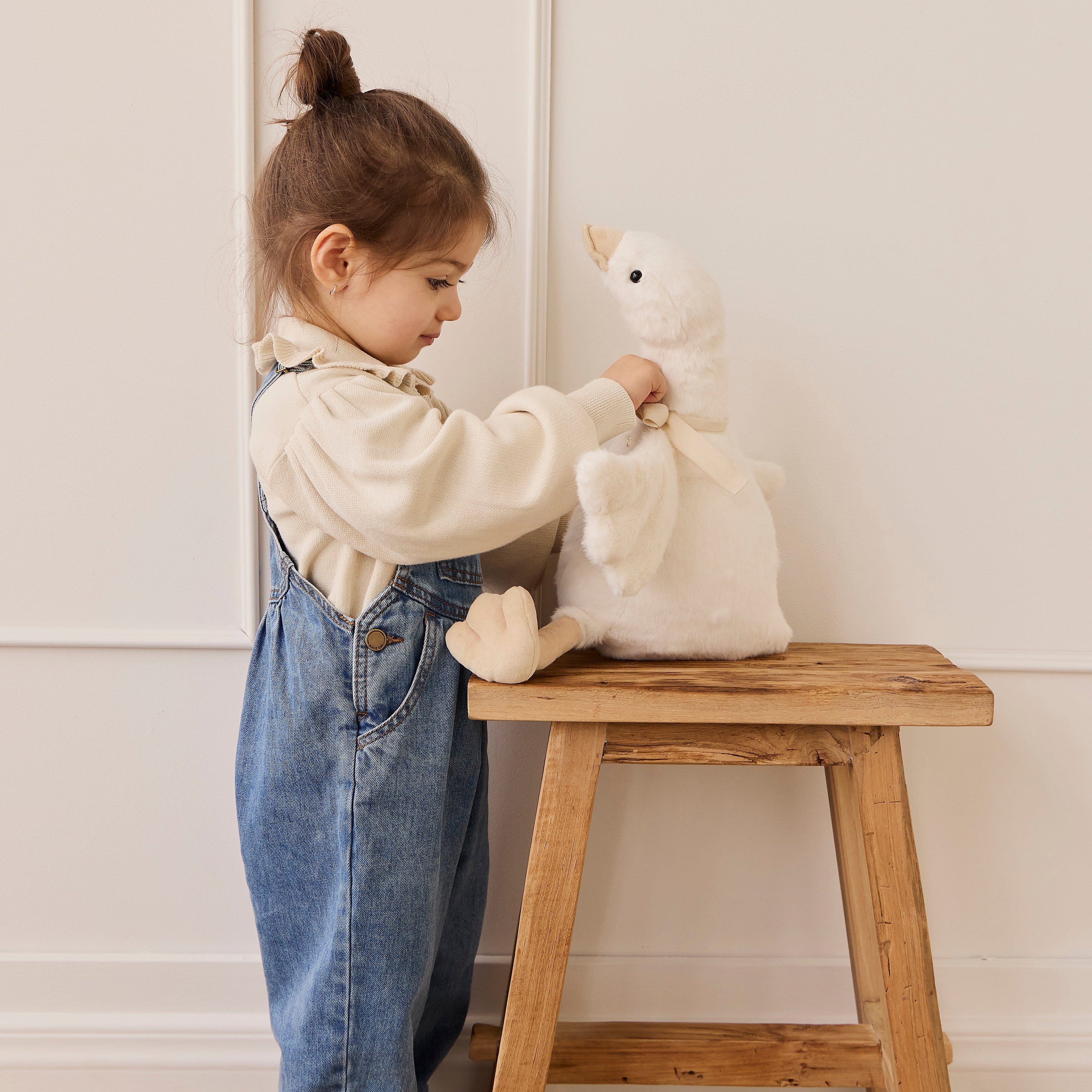 Child playing with a plush toy on a wooden stool against a white wall.