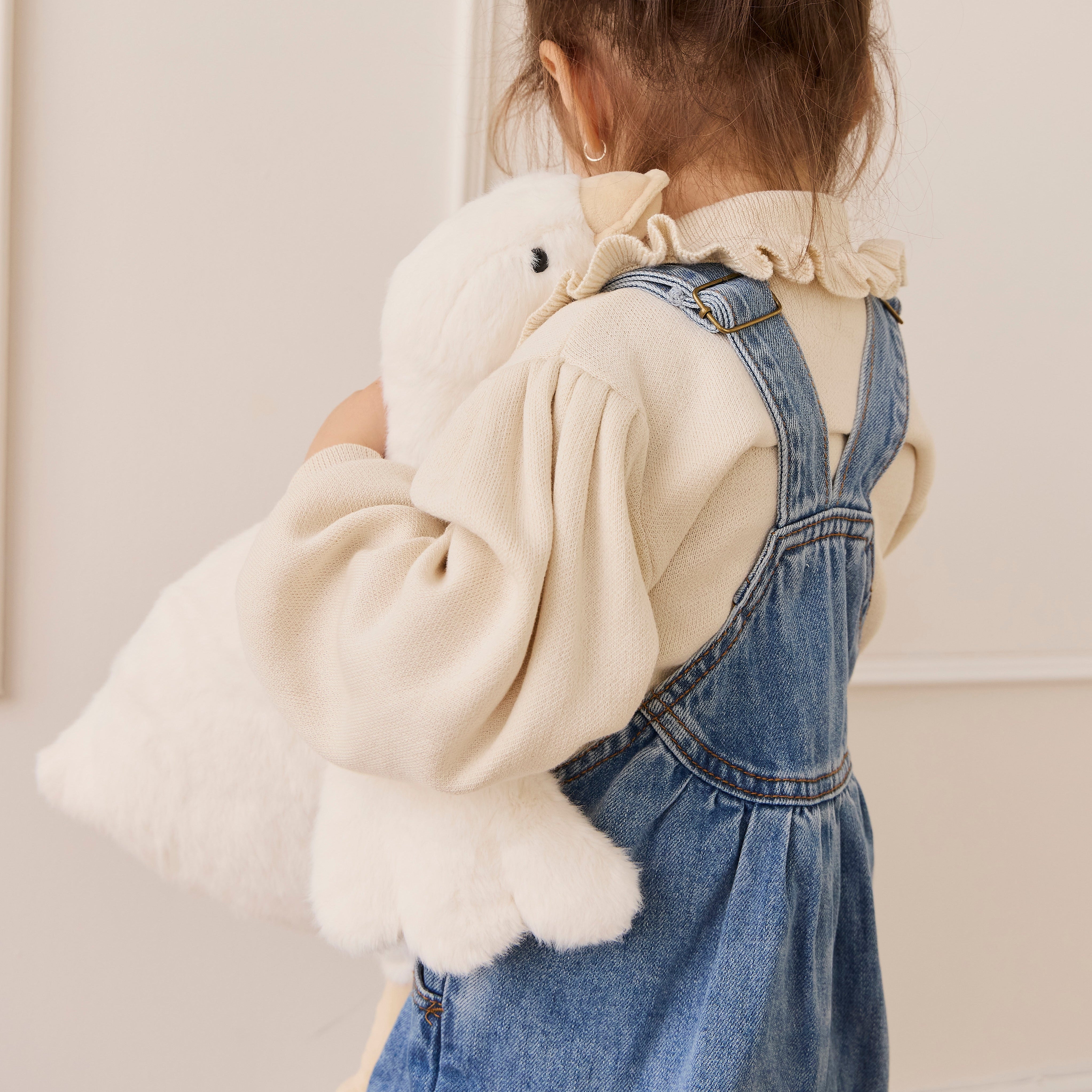 Child wearing a denim dress with a white fluffy bag, standing against a plain background