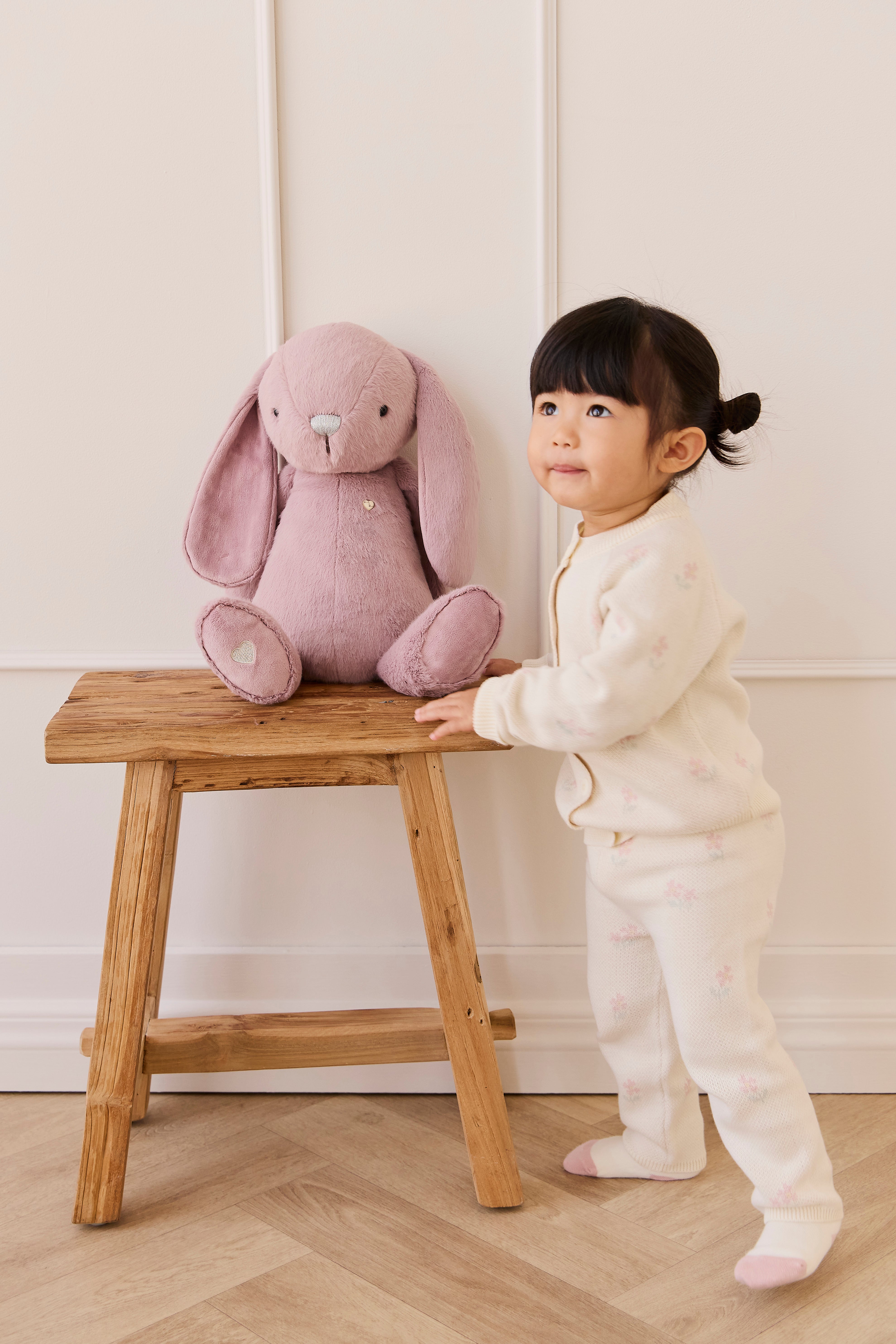 Child standing next to a wooden stool with a pink plush bunny on it.