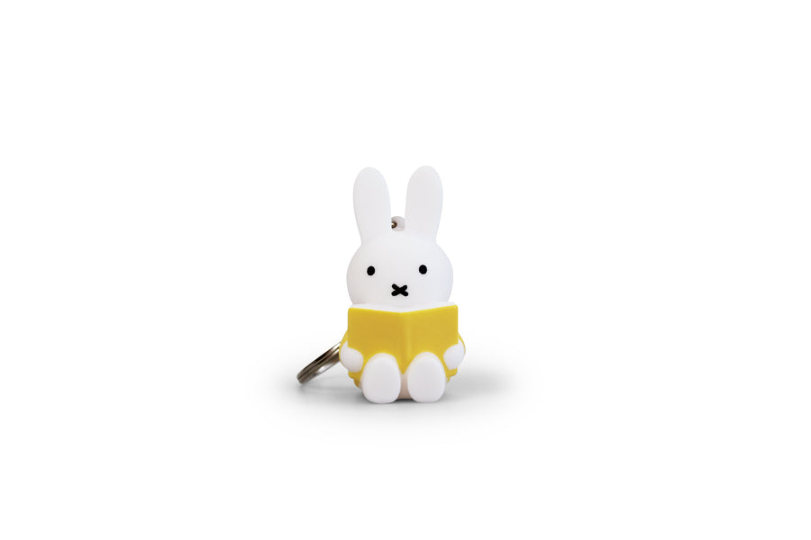 White Miffy bunny keychain, reading a yellow book.