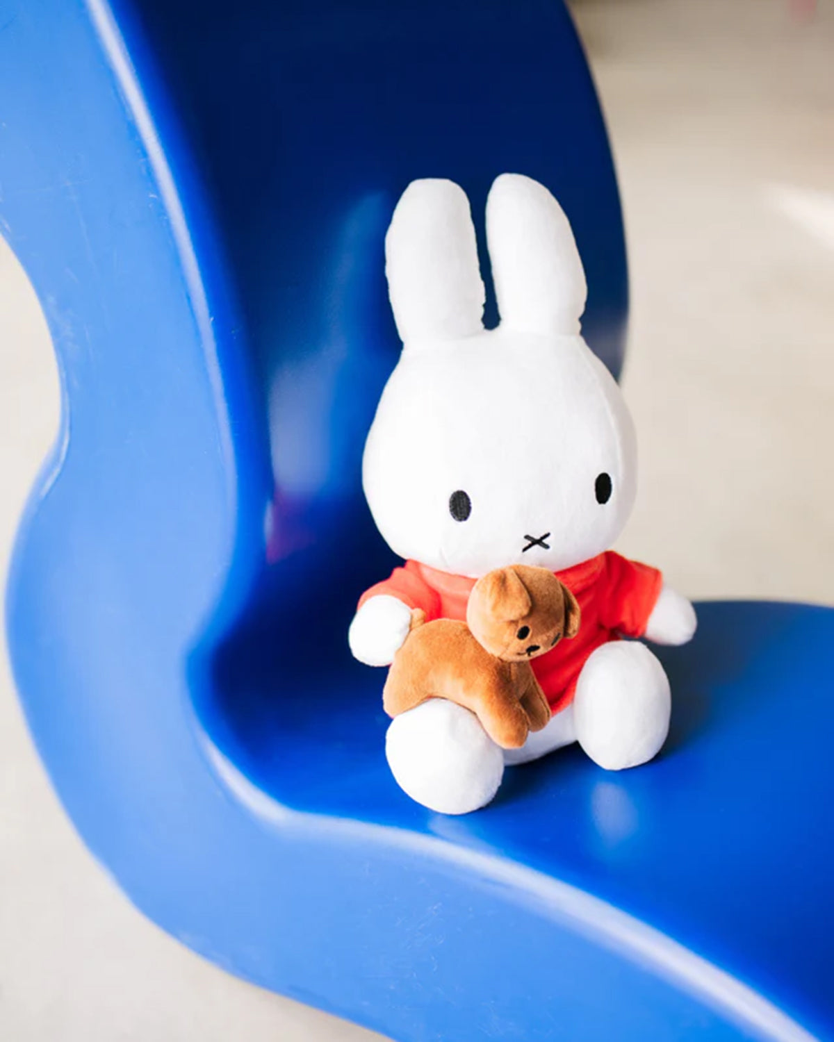 Stuffed white bunny with a red shirt holding a stuffed brown dog on a blue chair.