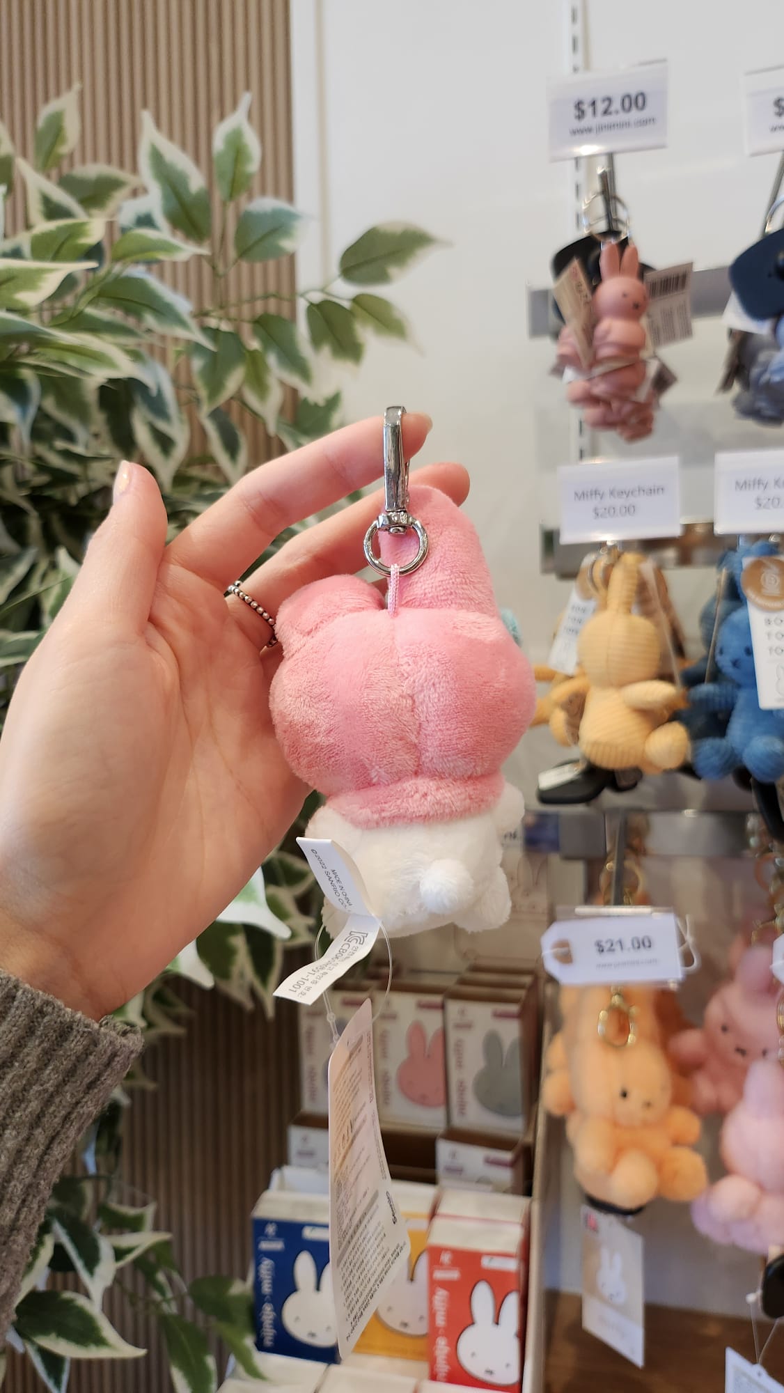 Hand holding a pink and white Miffy keychain in a store, with other Miffy keychains on display in the background.