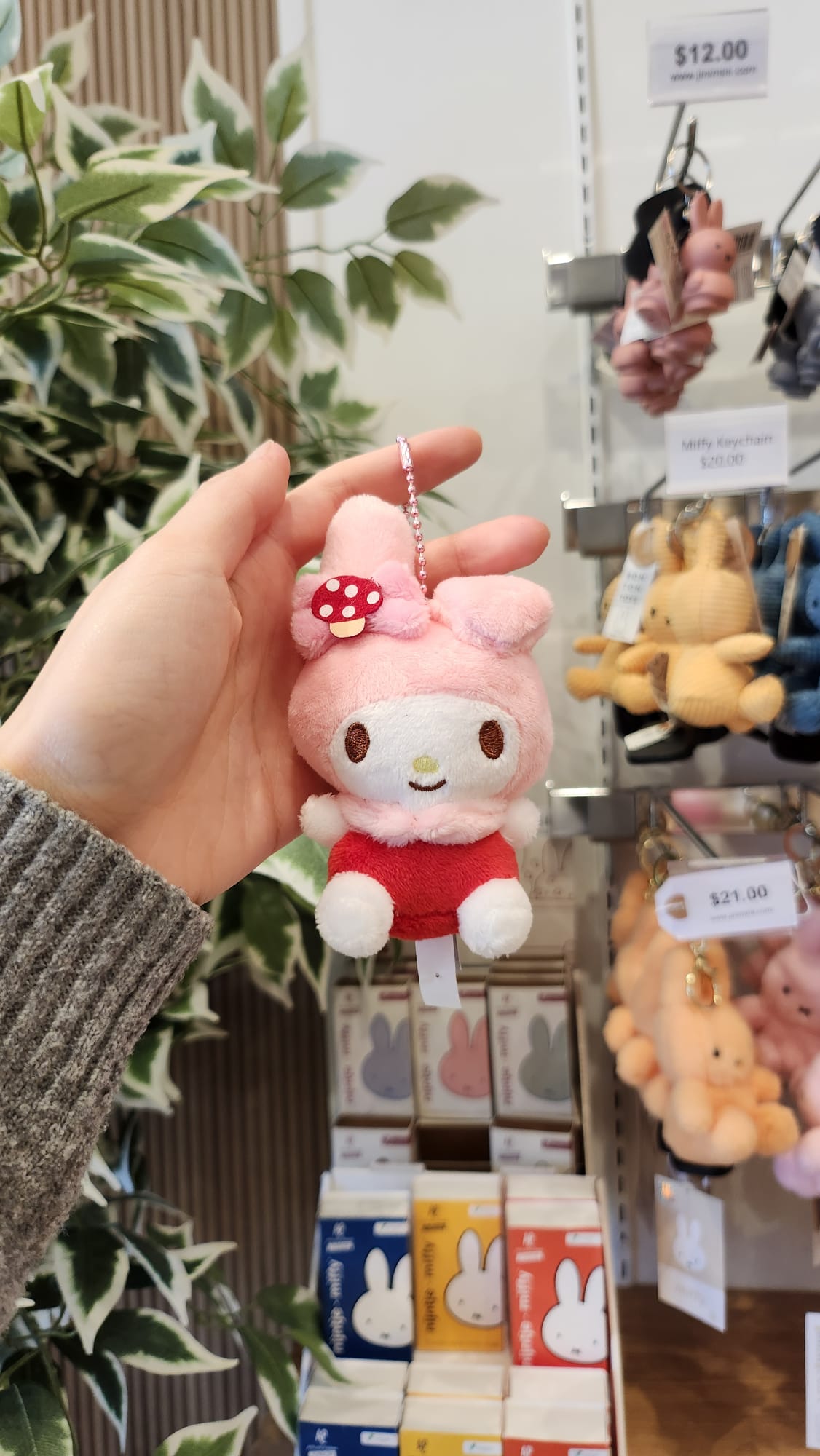 A person holding a pink My Melody keychain in front of a shelf with Miffy merchandise.