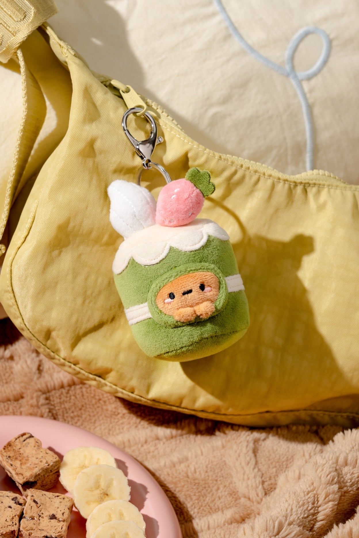 Plush keychain shaped like a green cup with a face, attached to a yellow bag.