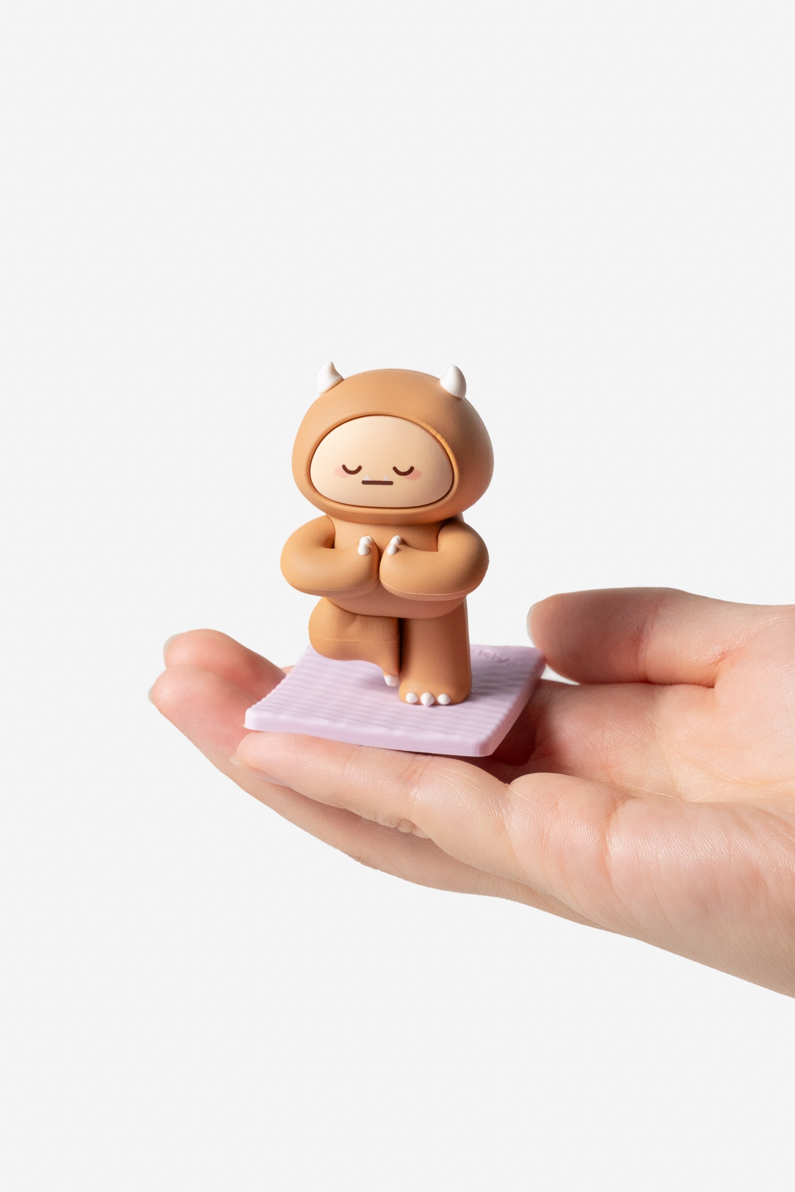 A brown cartoon monster figure in yoga pose on a purple mat, held in a hand.