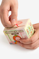 Hands opening a Kawawa Turtles blind box with a red seal.