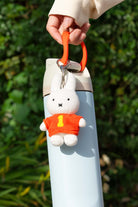 Person holding blue water bottle with Miffy plush keychain with orange shirt and the number one.