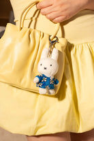 Person holding a yellow leather handbag with a Miffy plush keychain.