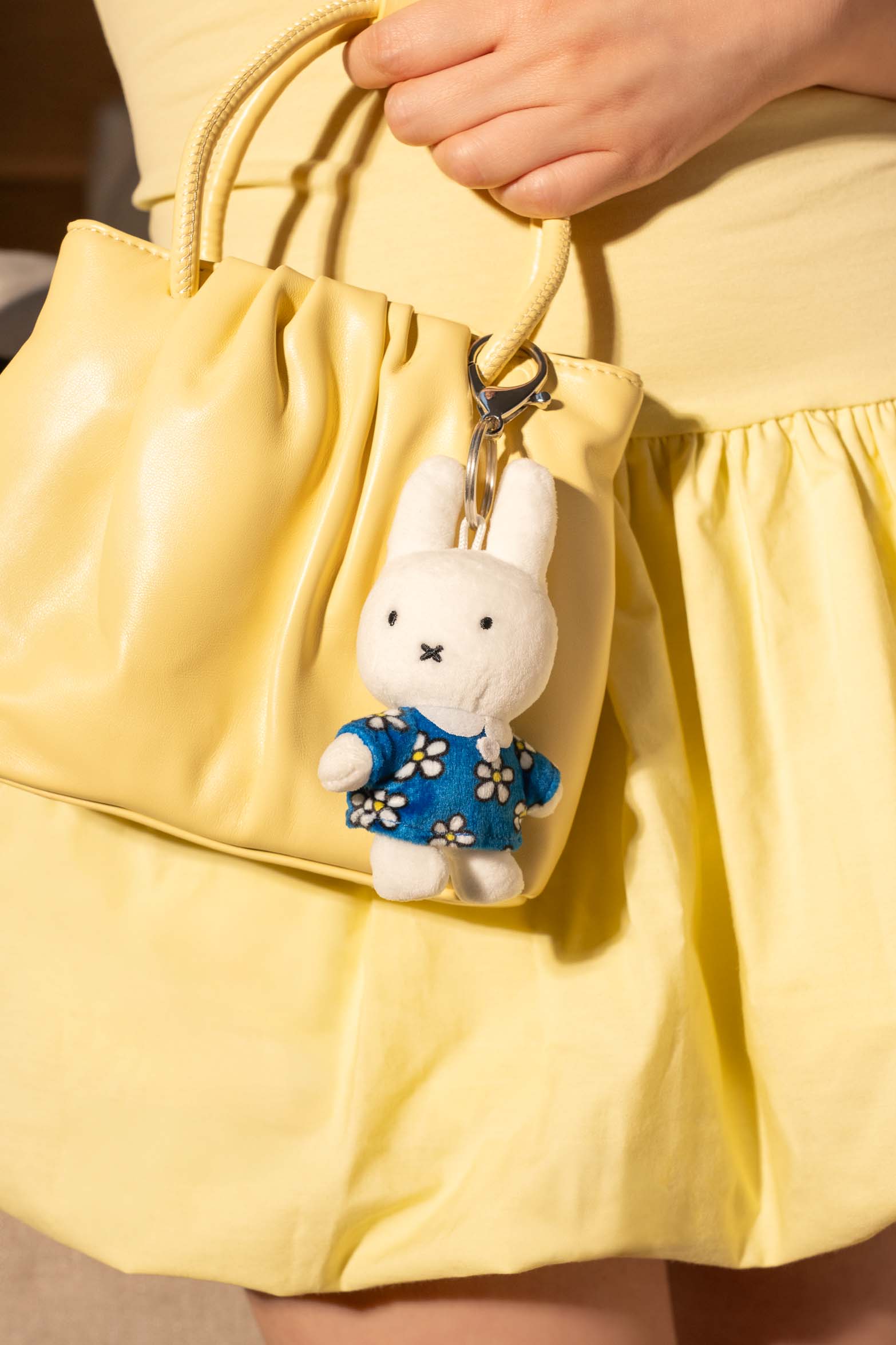 Person holding a yellow leather handbag with a Miffy plush keychain.
