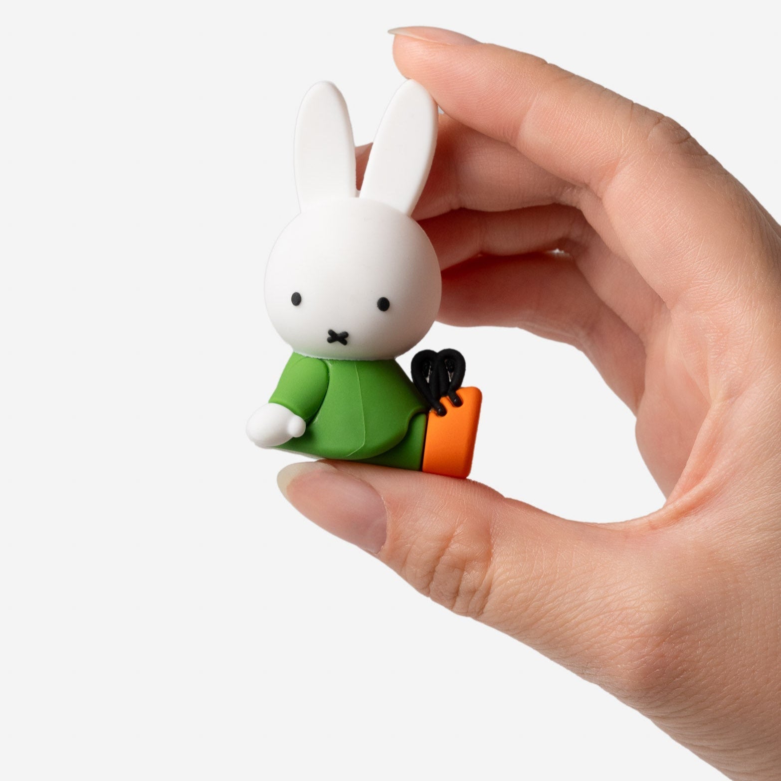 Hand holding a small Miffy figurine wearing a green outfit and orange boots.