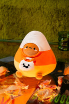 Plush candy corn toy with a smiling face on a table with wrapped caramels.