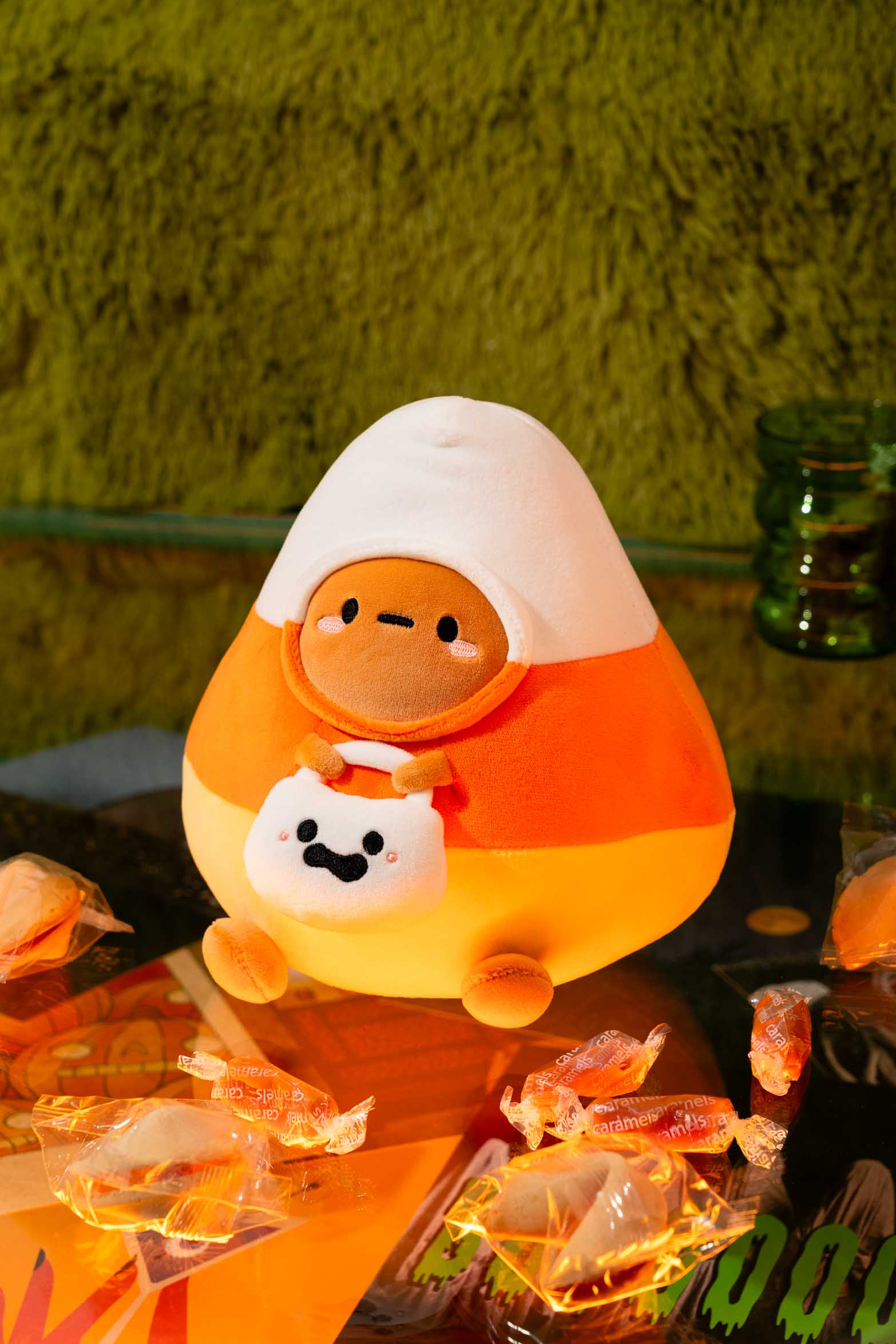 Plush candy corn toy with a smiling face on a table with wrapped caramels.