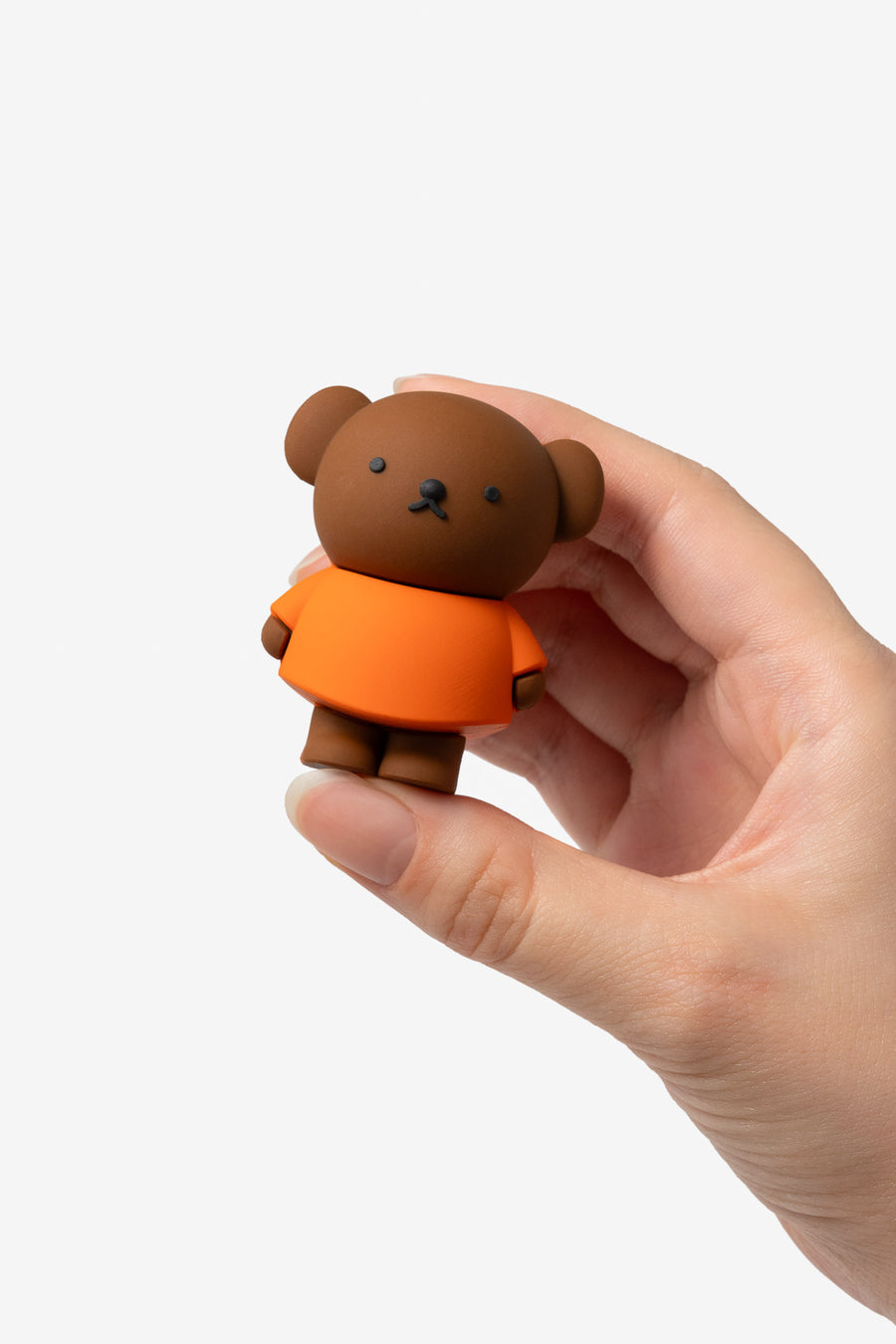 Small brown bear figurine wearing an orange shirt held in a hand against a white background