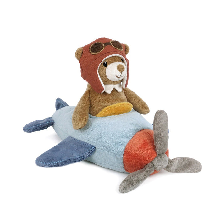 Plush toy bear in an aviator hat sitting on a toy airplane on a white background