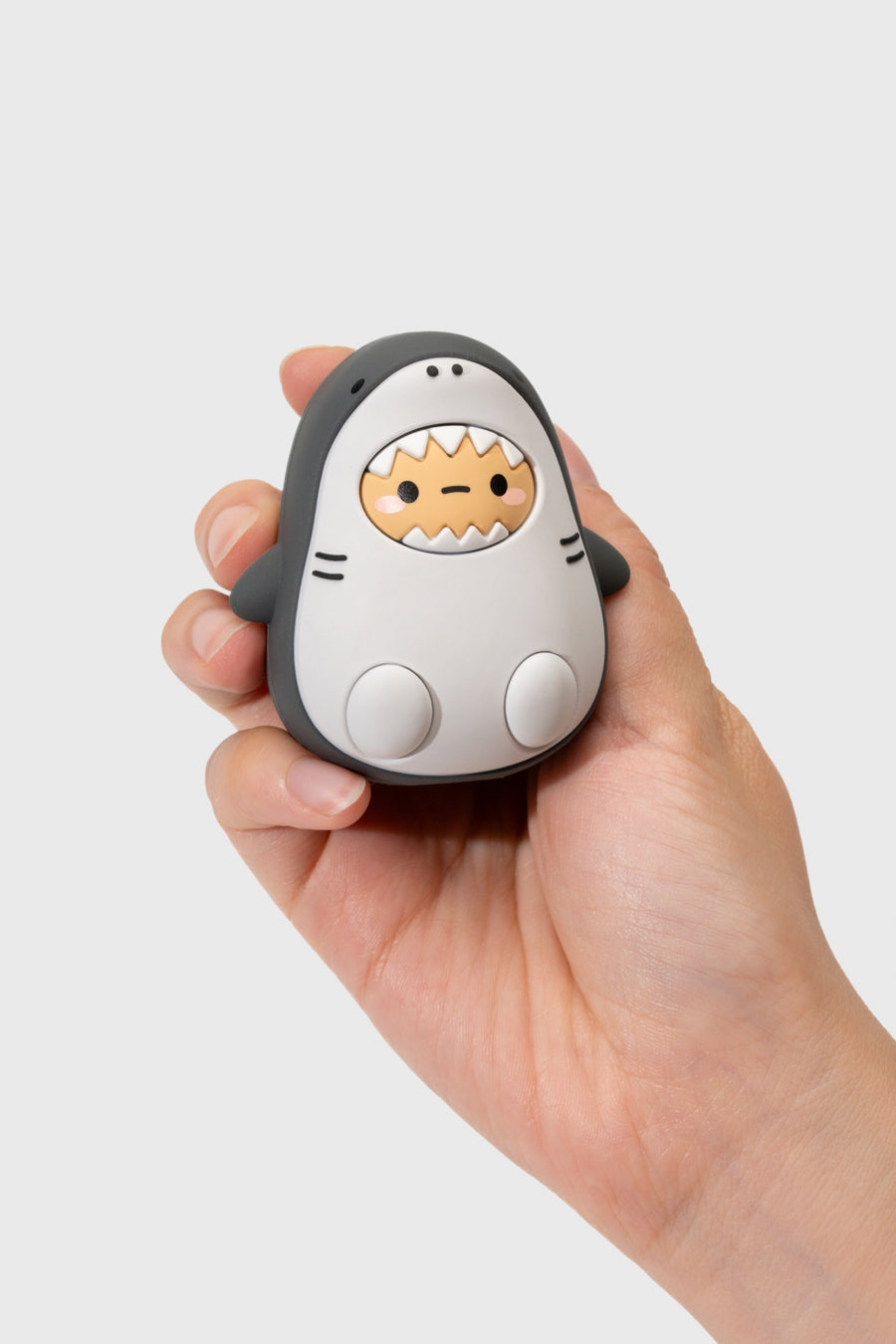 Hand holding a small, cute shark-shaped device with a cartoon face on a light gray background