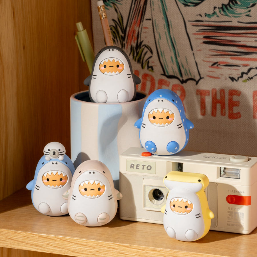 Set of cartoon shark figurines on a shelf with a retro camera and tropical-themed fabric in the background.