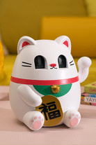 White maneki-neko figurine with a red collar, green bib, gold bell, and gold coin featuring black Japanese characters.