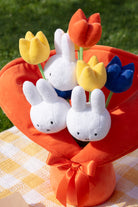 Stuffed Miffy bunny heads and fabric tulips in an orange fabric vase with a ribbon, on a yellow and white checkered picnic blanket.