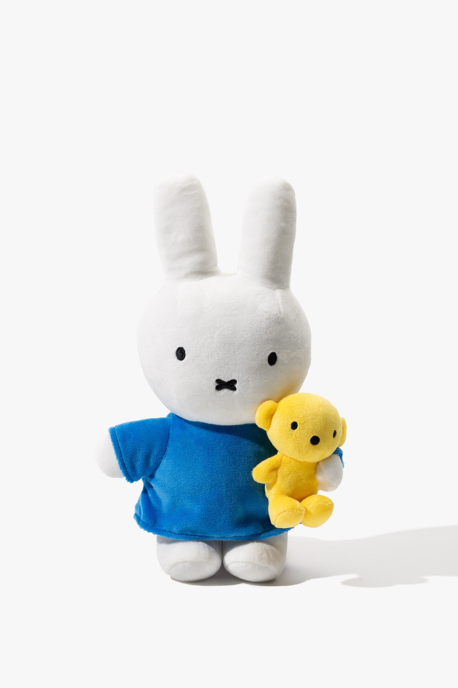 White Miffy plush toy in blue shirt holding yellow bear.