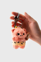 Hand holding a plush pink bear keychain with a yellow polka dot skirt and a brown bone.