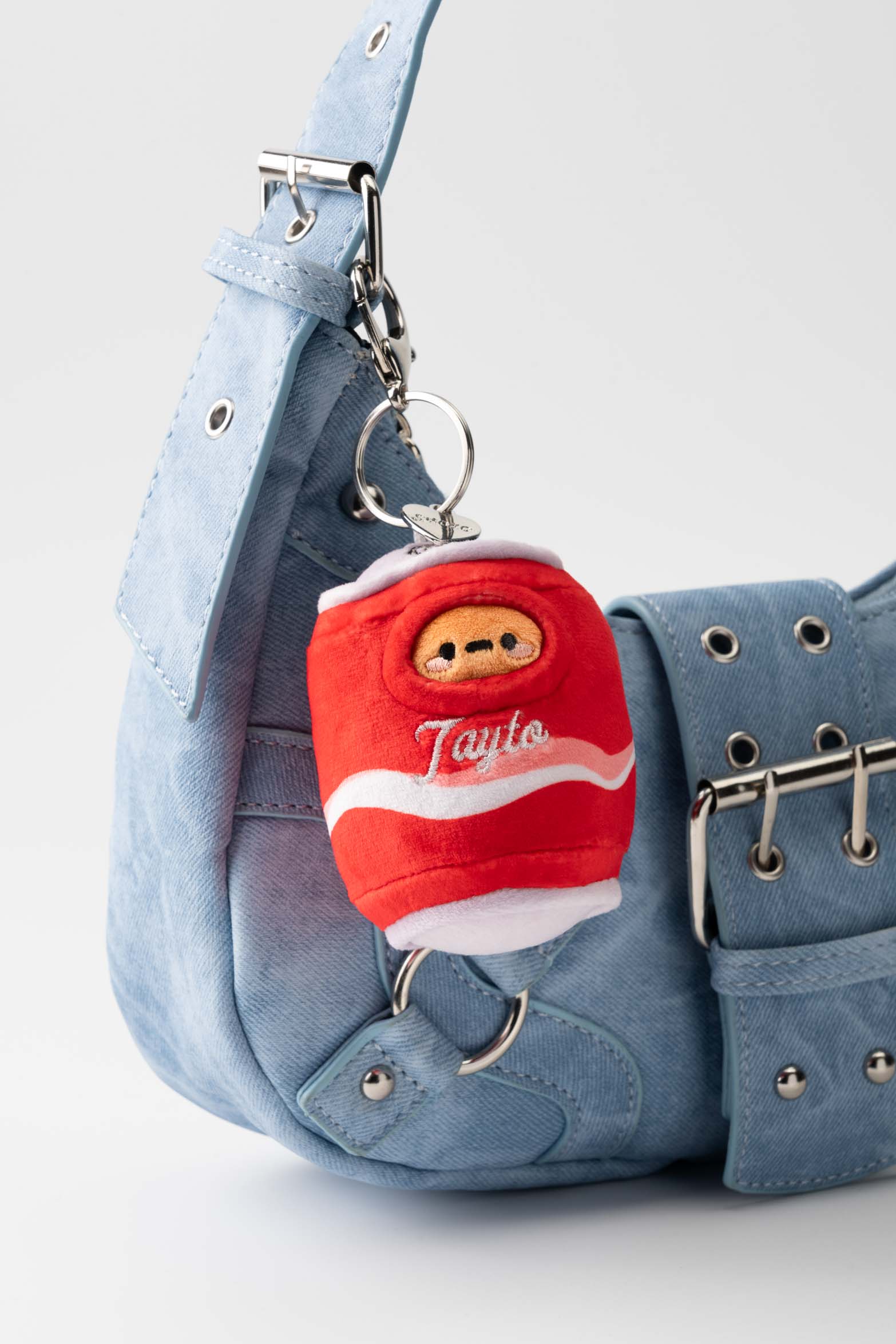 Close-up of light blue denim purse with a red and white plush drink keychain.