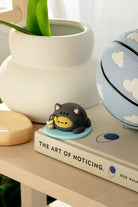 Cat figurine holding bubble tea on "The Art of Noticing" book, next to a blue basketball with white cloud design.