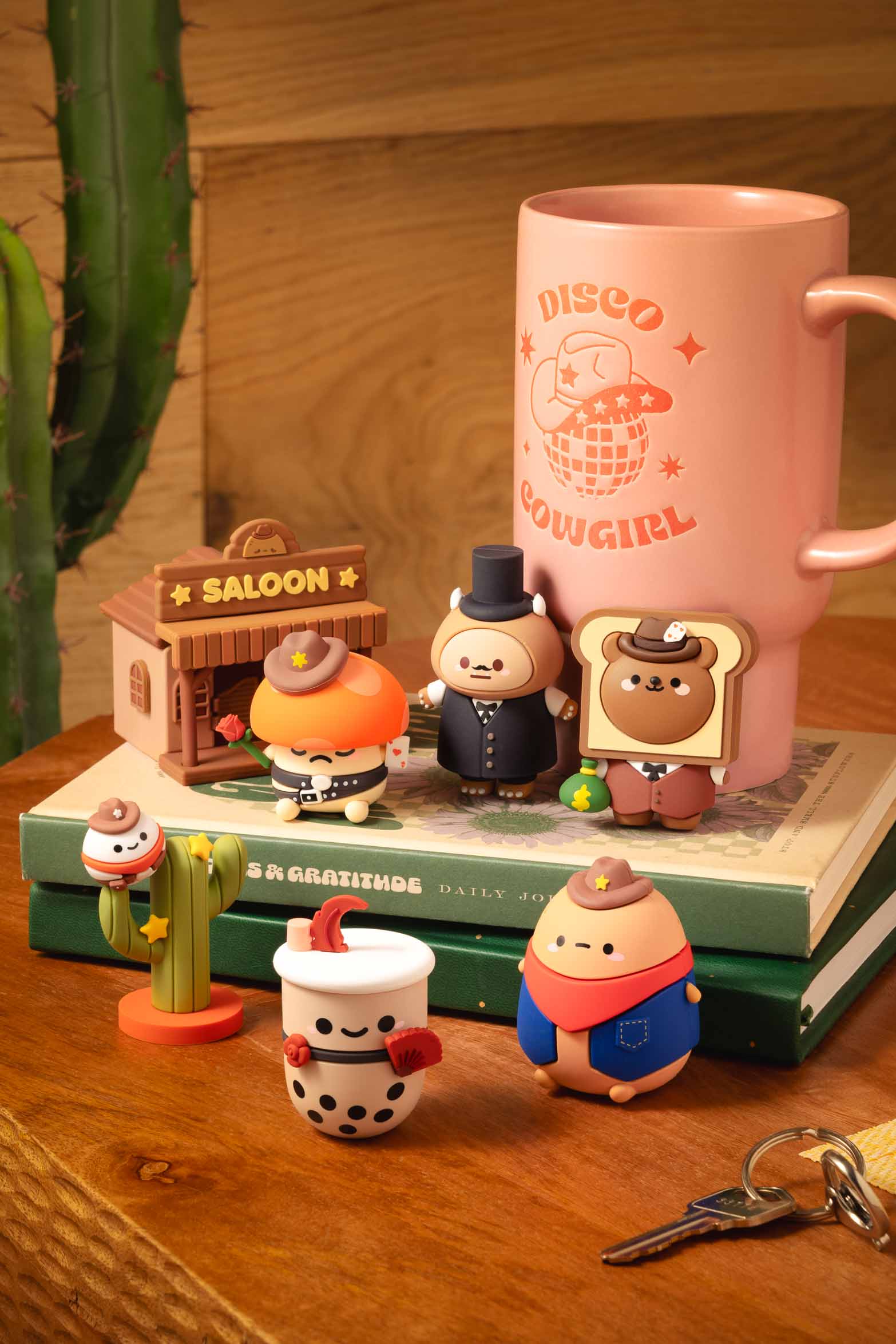 A collection of stylized cartoon cowboy figurine toys on a wooden surface with cactus, books, and mug.