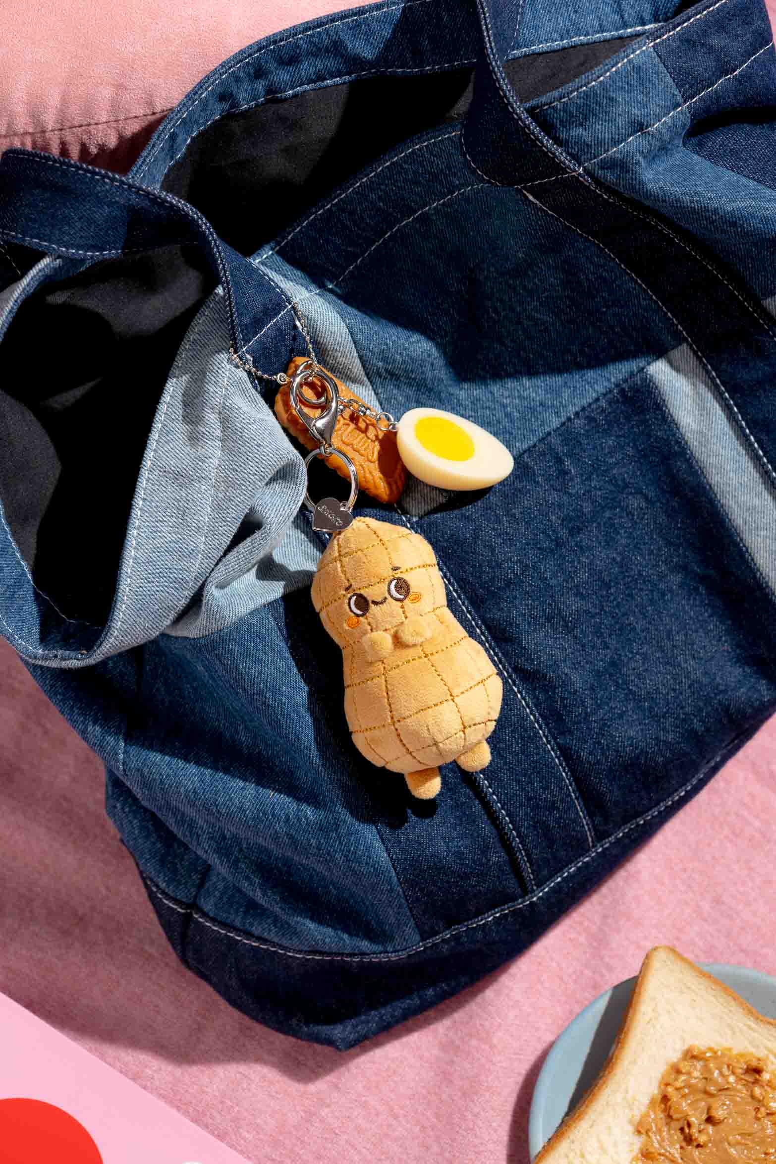 Denim patchwork tote bag with cute plush peanut keychain, egg, and cookie charm. A peanut butter toast plate is in the bottom right corner.