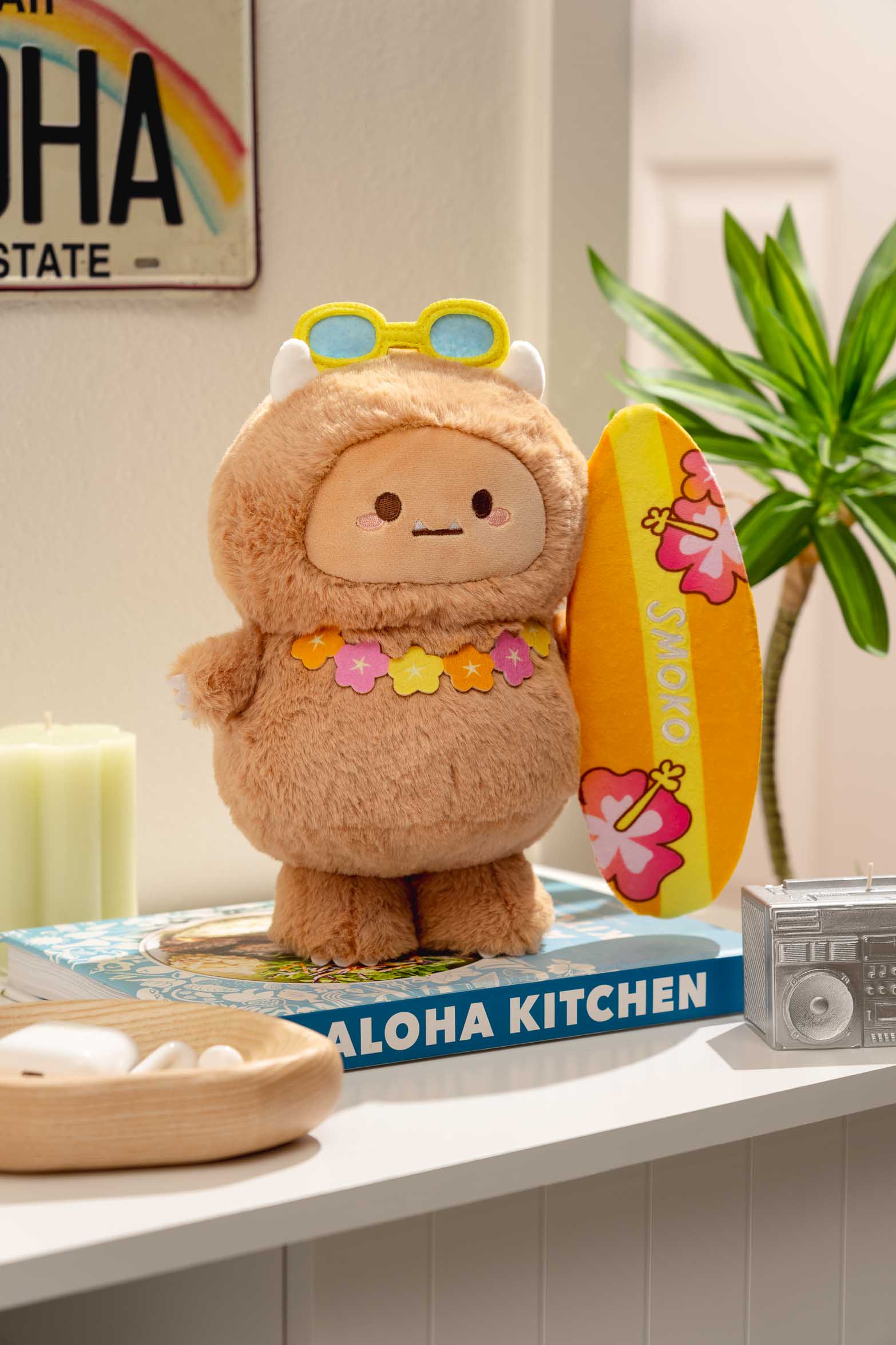 Plush toy monster with a lei, sunglasses, and surfboard standing on a cookbook.