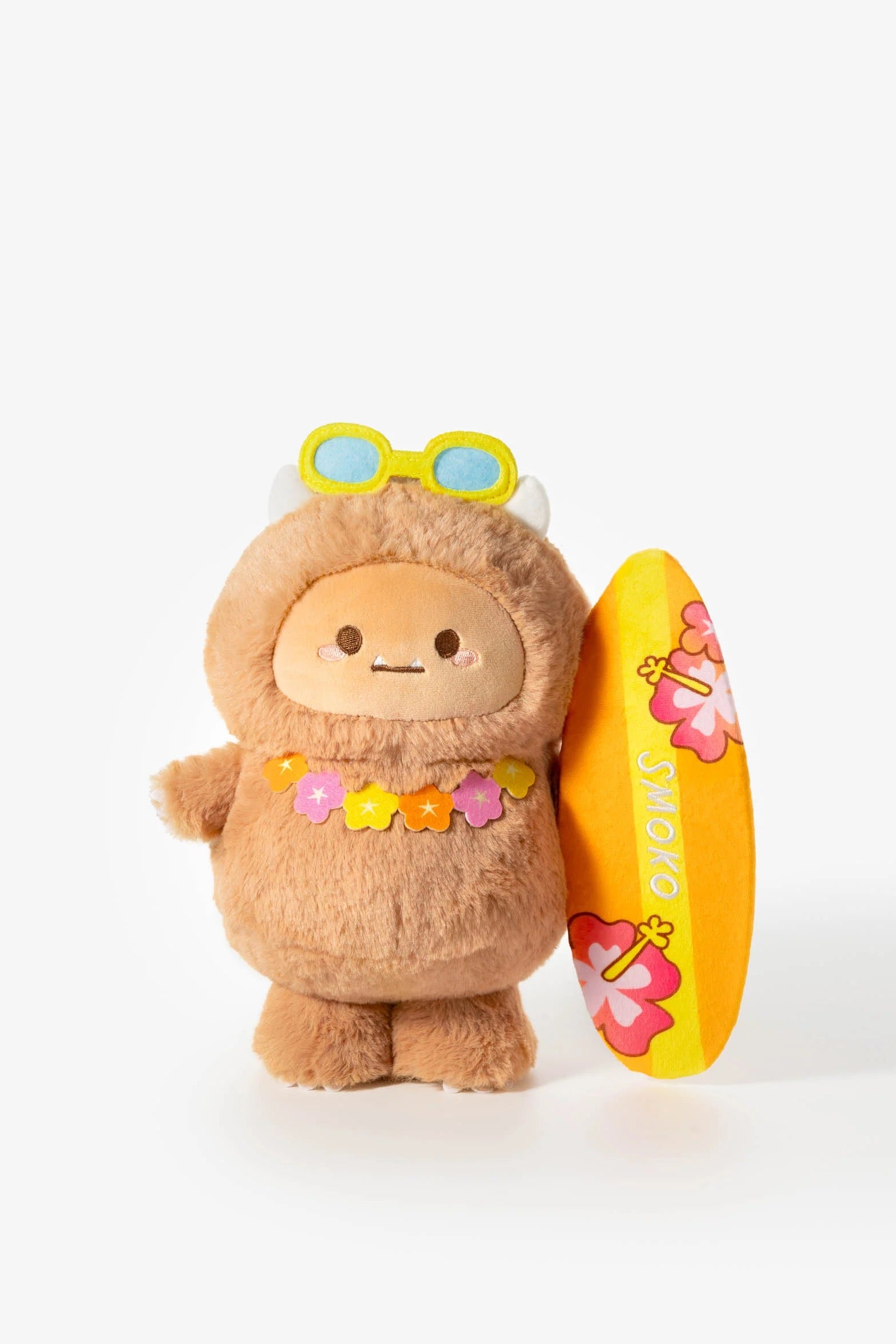 Brown stuffed yeti toy with a yellow surfboard, flower lei, and sunglasses.
