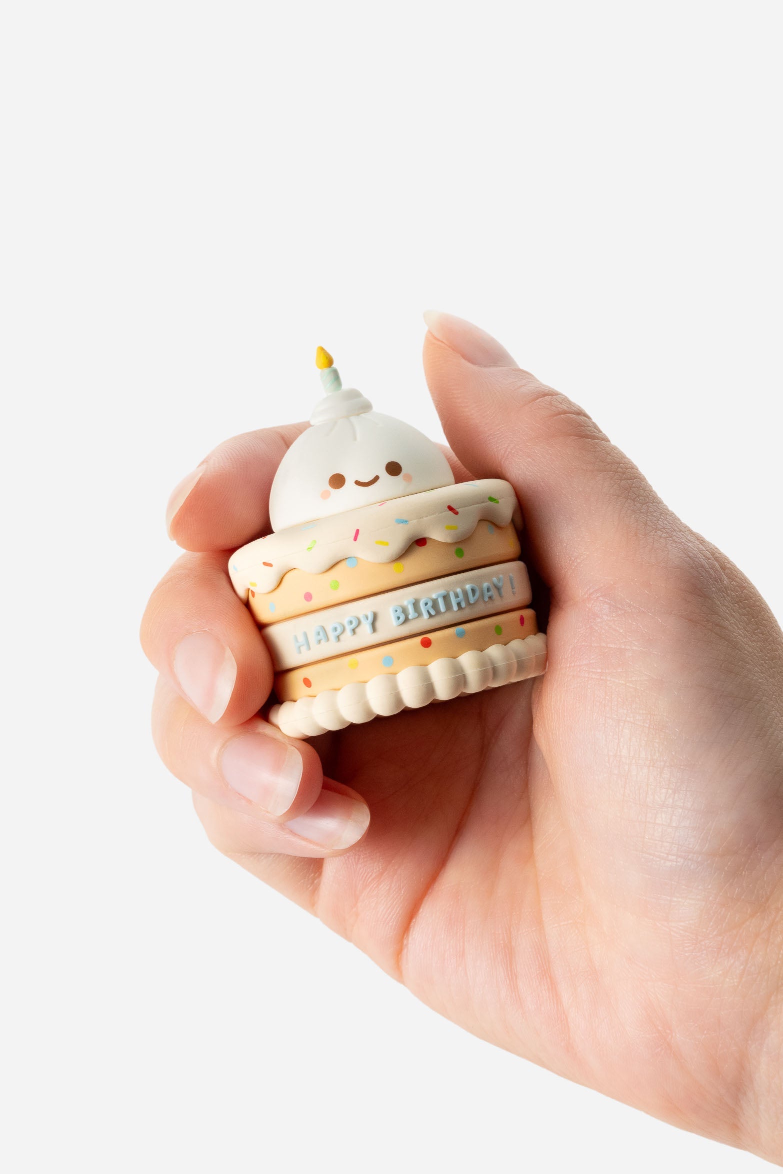 Hand holding a small, cartoonish birthday cake with a candle.