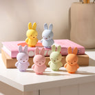 Six pastel-colored Miffy bunny figures on a pink book on a beige surface.