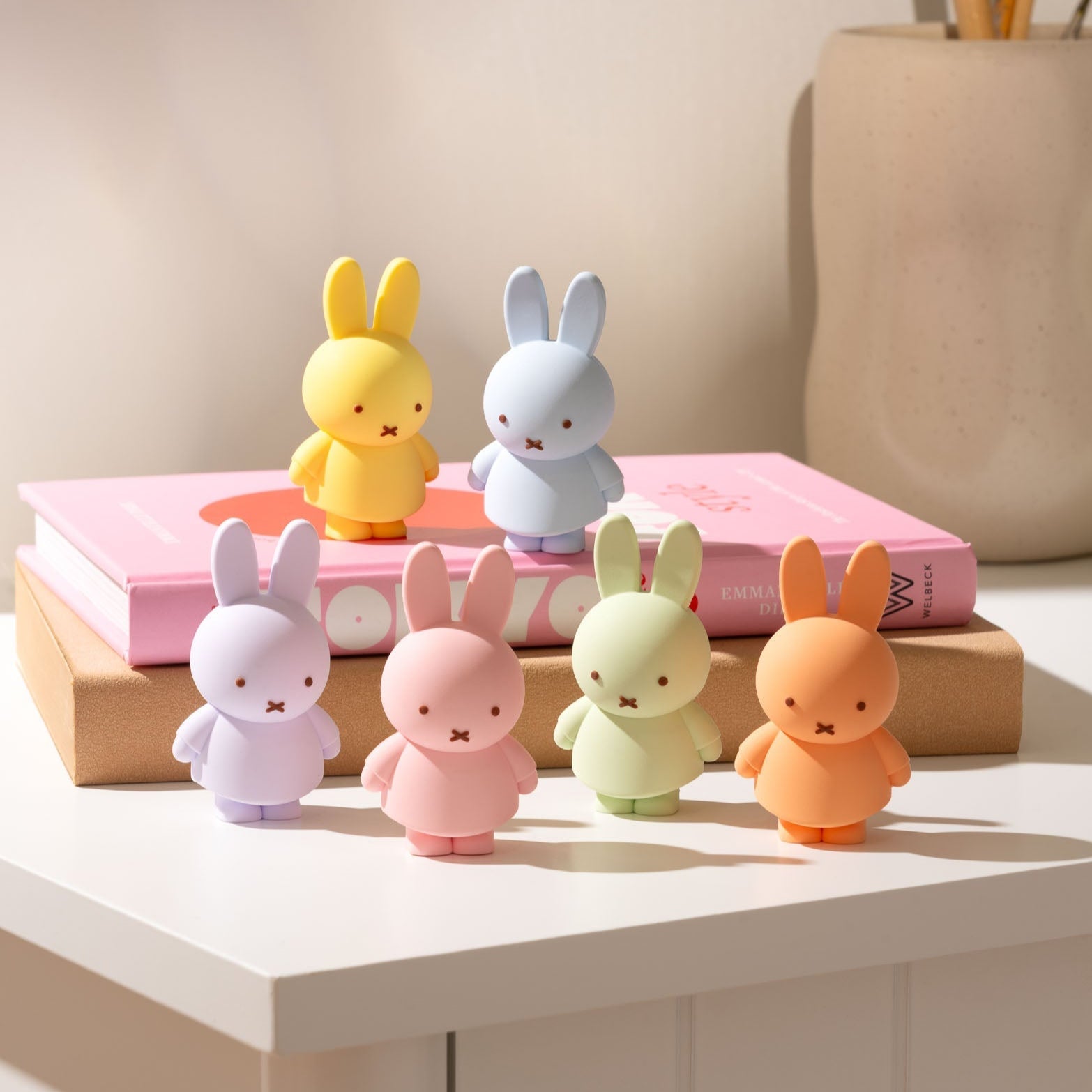 Six pastel-colored Miffy bunny figures on a pink book on a beige surface.