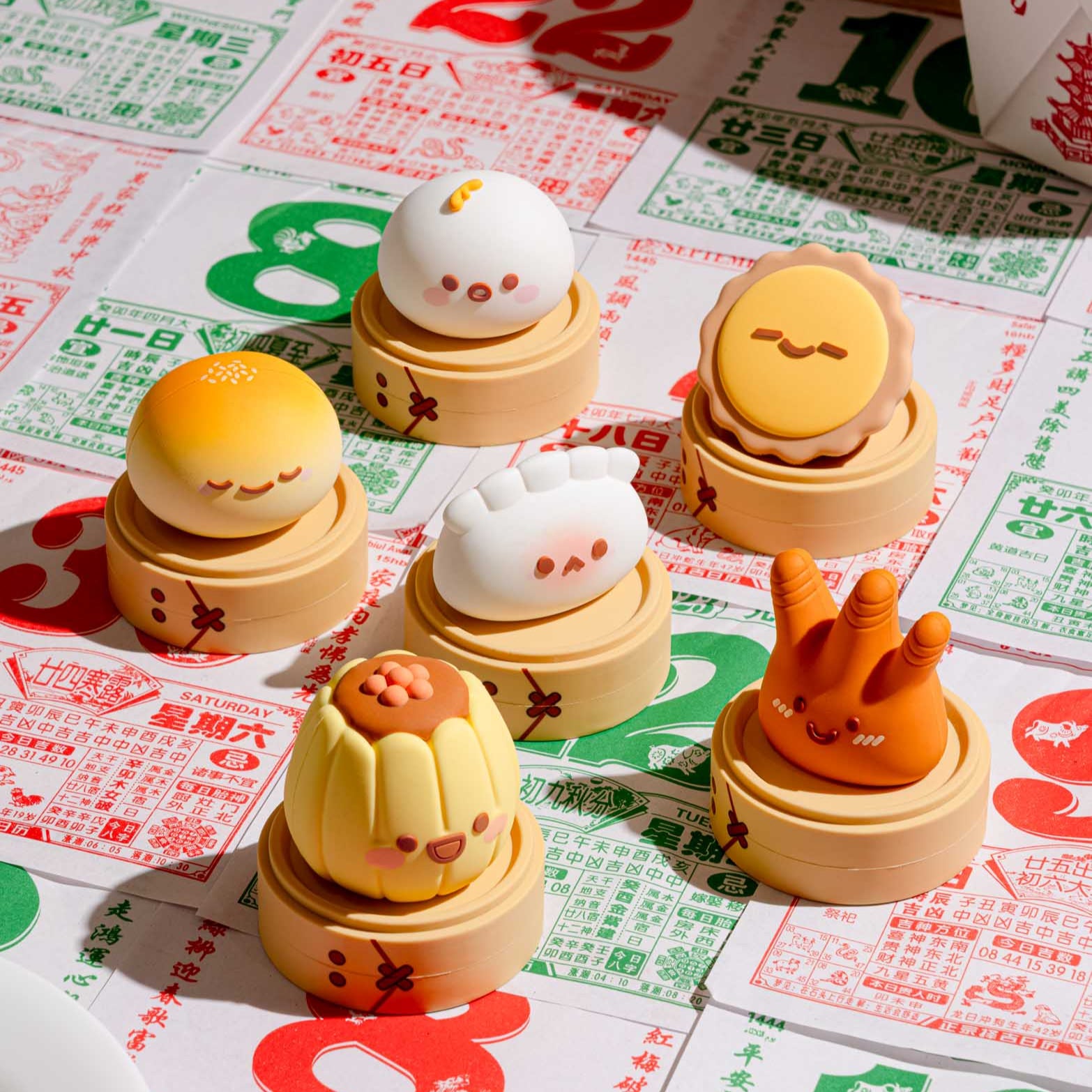 Six cute dim sum character figurines in steamer baskets on a table covered in Chinese newspaper.
