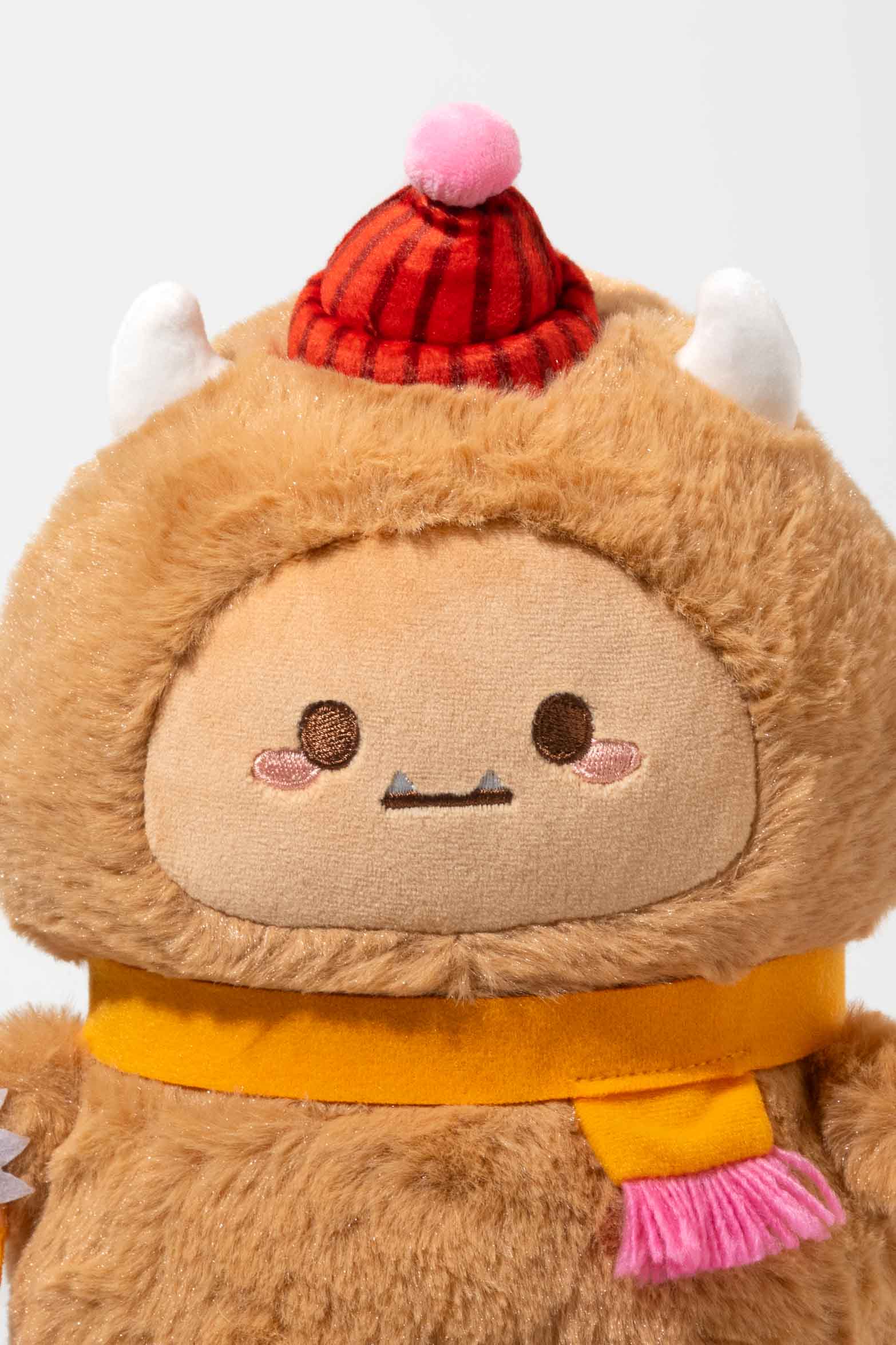 Stuffed monster toy wearing a red hat and yellow scarf.