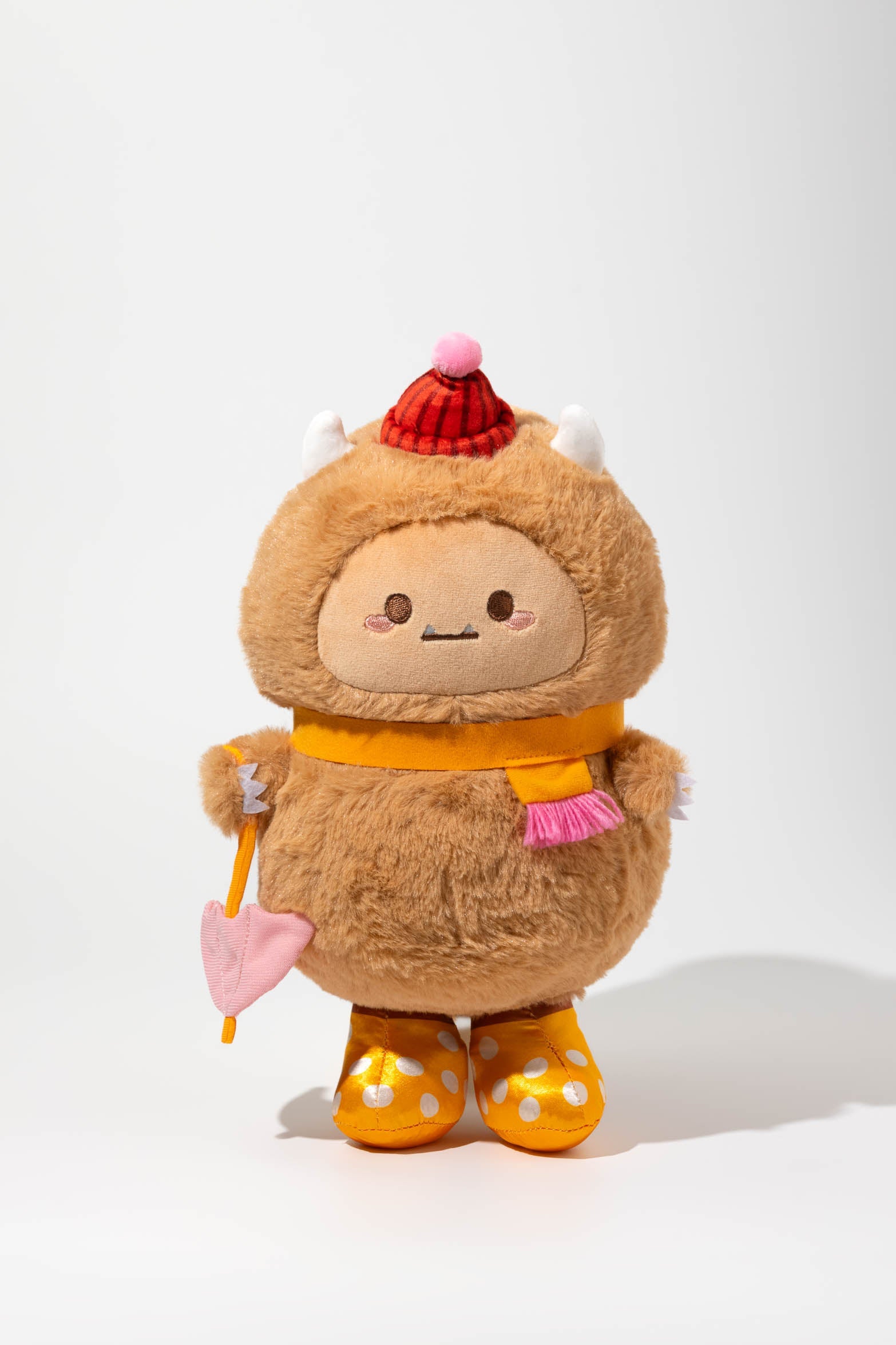 Stuffed brown monster toy with red hat, yellow scarf, and polka-dotted gold boots.