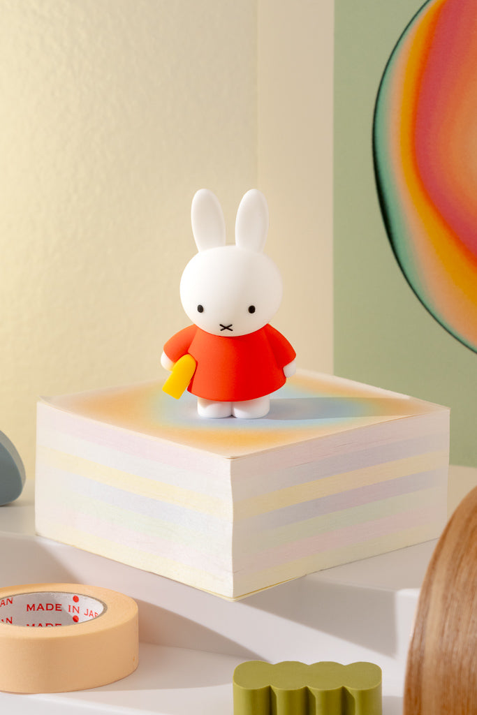 White rabbit figurine in a red outfit on a colorful block with a yellow object